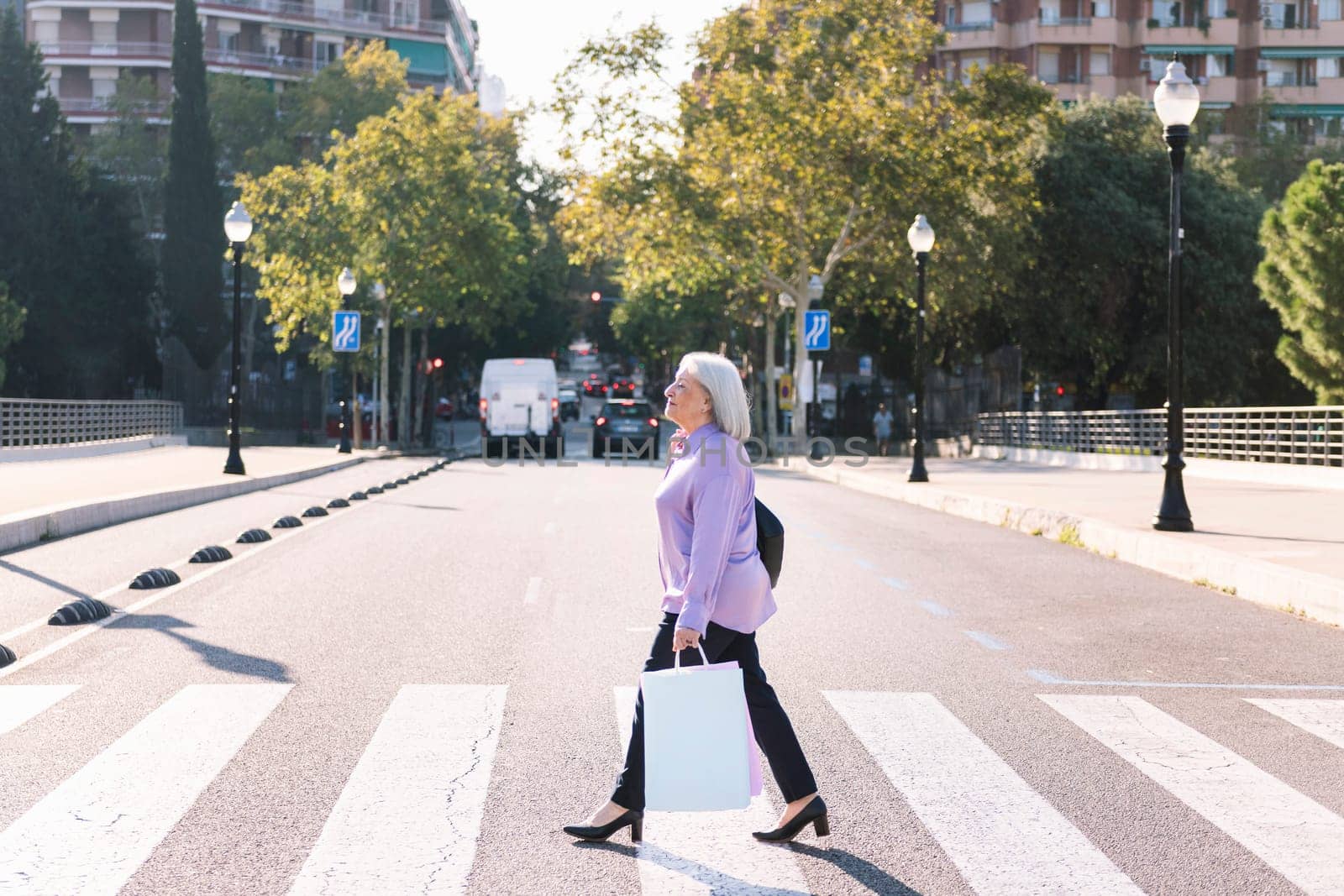 senior woman crossing a city street at a pedestrian crossing with shopping bags in her hand, concept of elderly people leisure and active lifestyle