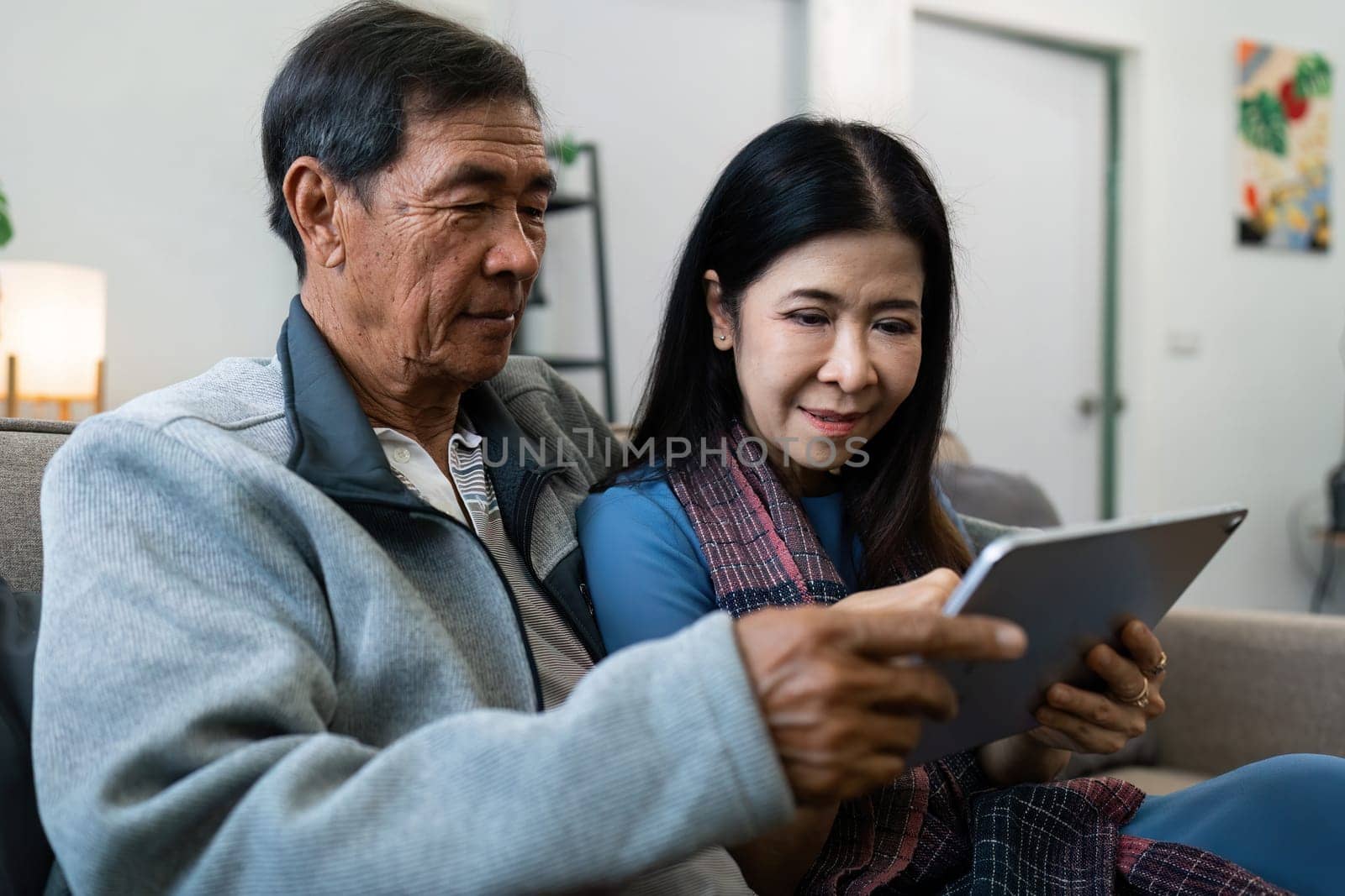 Retired elderly couple sits on couch using tablet together and relax in their home. Senior Activity Concept.