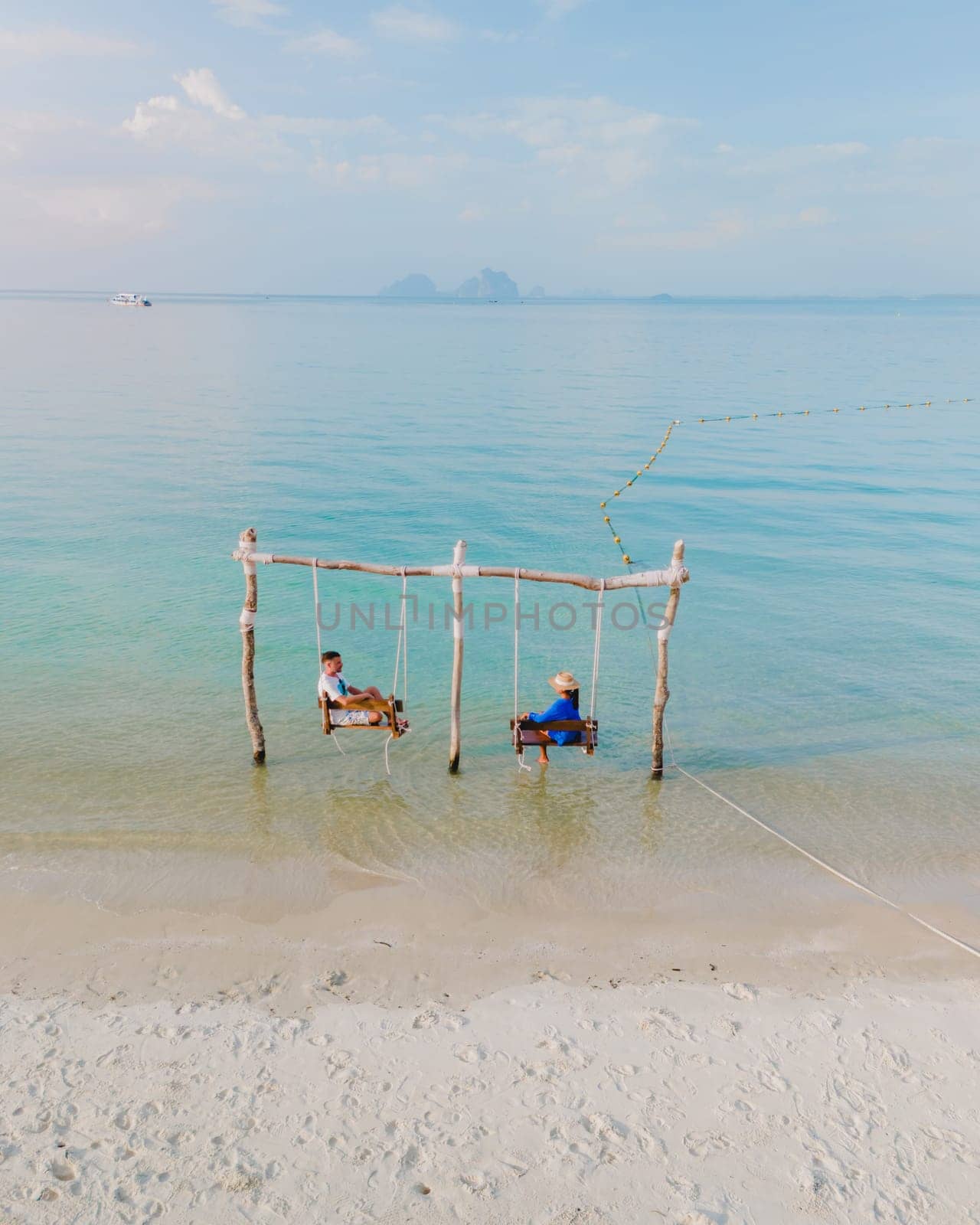 a couple of men and a woman on a swing at the beach of Koh Muk or Koh Mook Trang Thailand, a couple on a swing in the ocean
