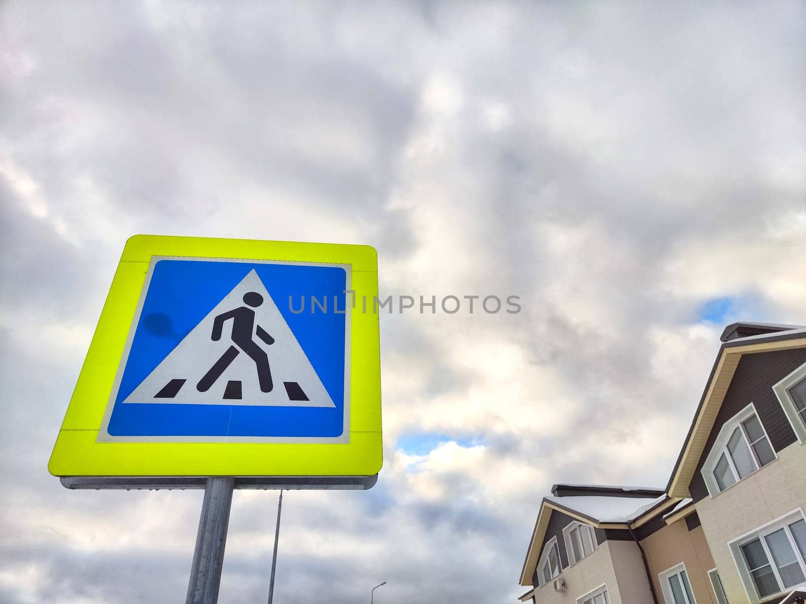 A pedestrian crossing sign on the background of a gray sky with clouds. Drawing, pictogram for pedestrians crossing the road