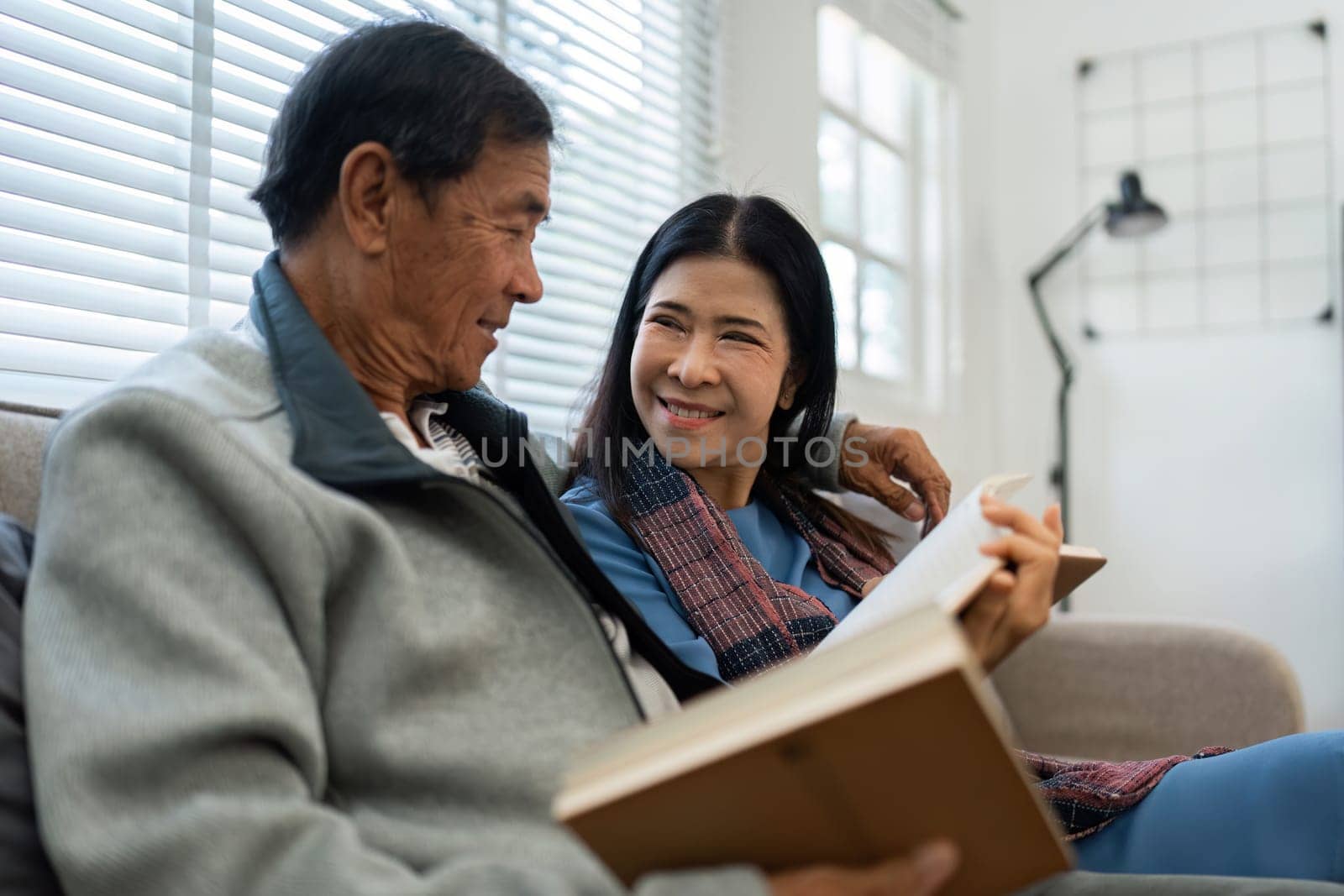 Retired elderly couple sits on couch in their home reading relaxing book. Senior Activity Concept.