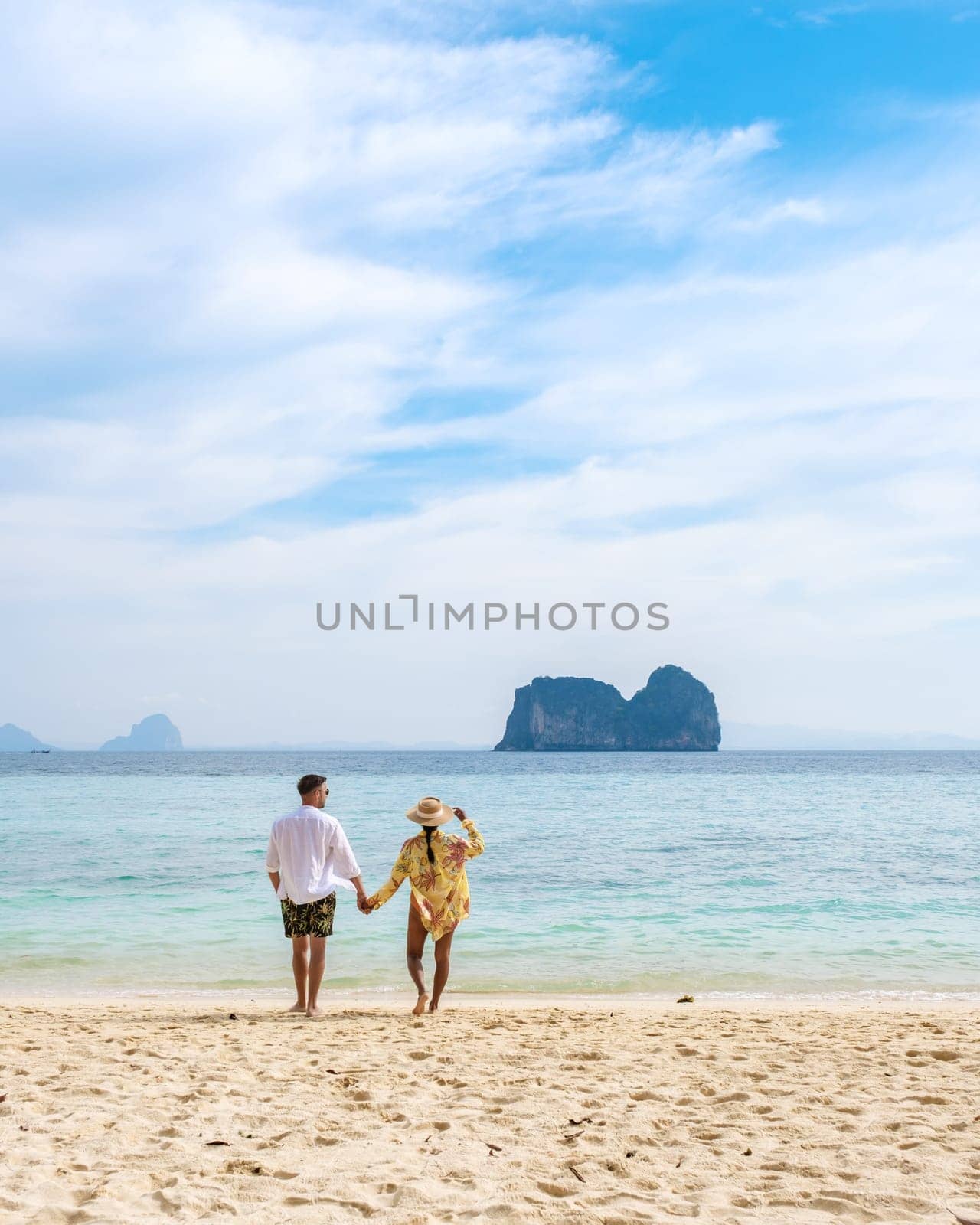 Happy young couple, an Asian woman and European man on the beach of Koh Ngai island, soft white sand, and a turqouse colored ocean in Koh Ngai Trang Thailand