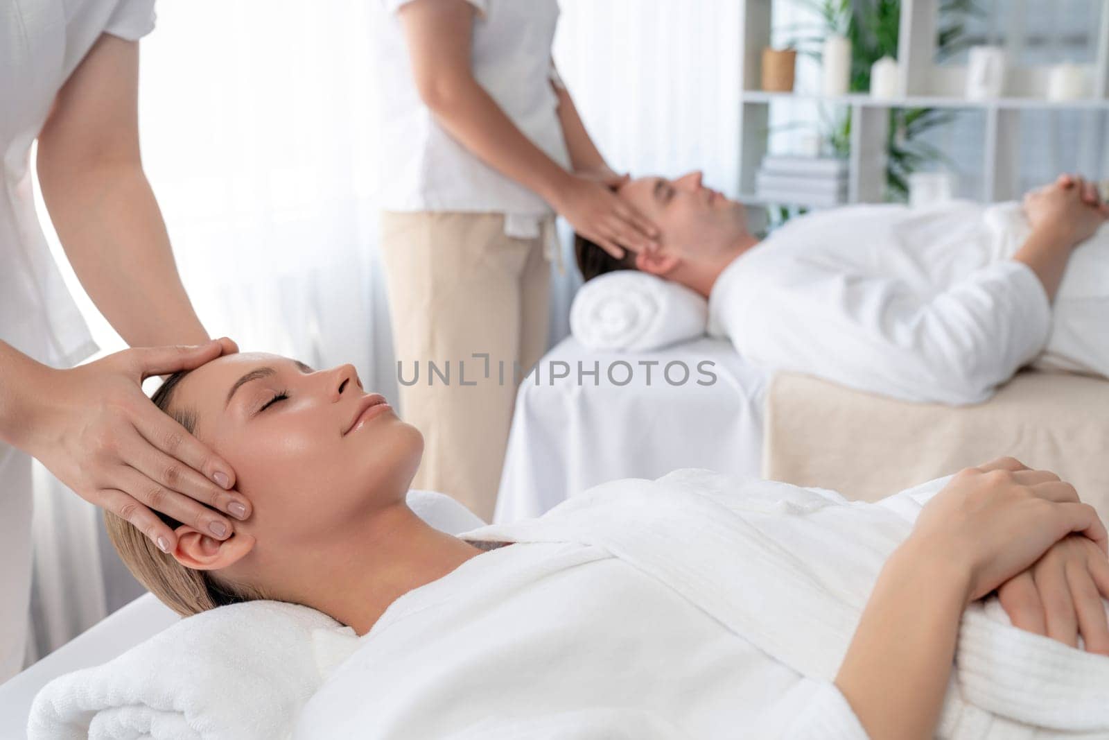 Caucasian couple enjoying relaxing anti-stress head massage and pampering facial beauty skin recreation leisure in dayspa modern light ambient at luxury resort or hotel spa salon. Quiescent