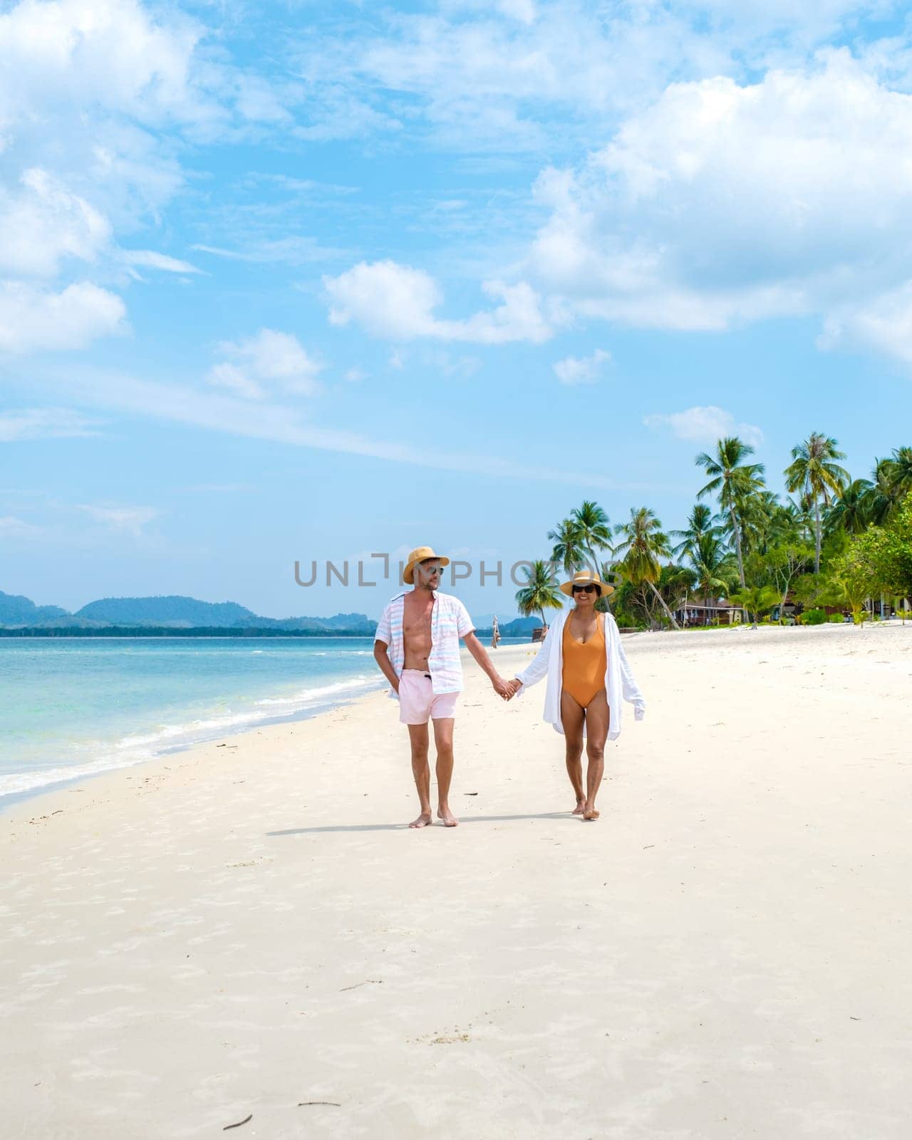 Koh Mook a young couple of caucasian men and Thai Asian woman walking at the beach in Thailand by fokkebok