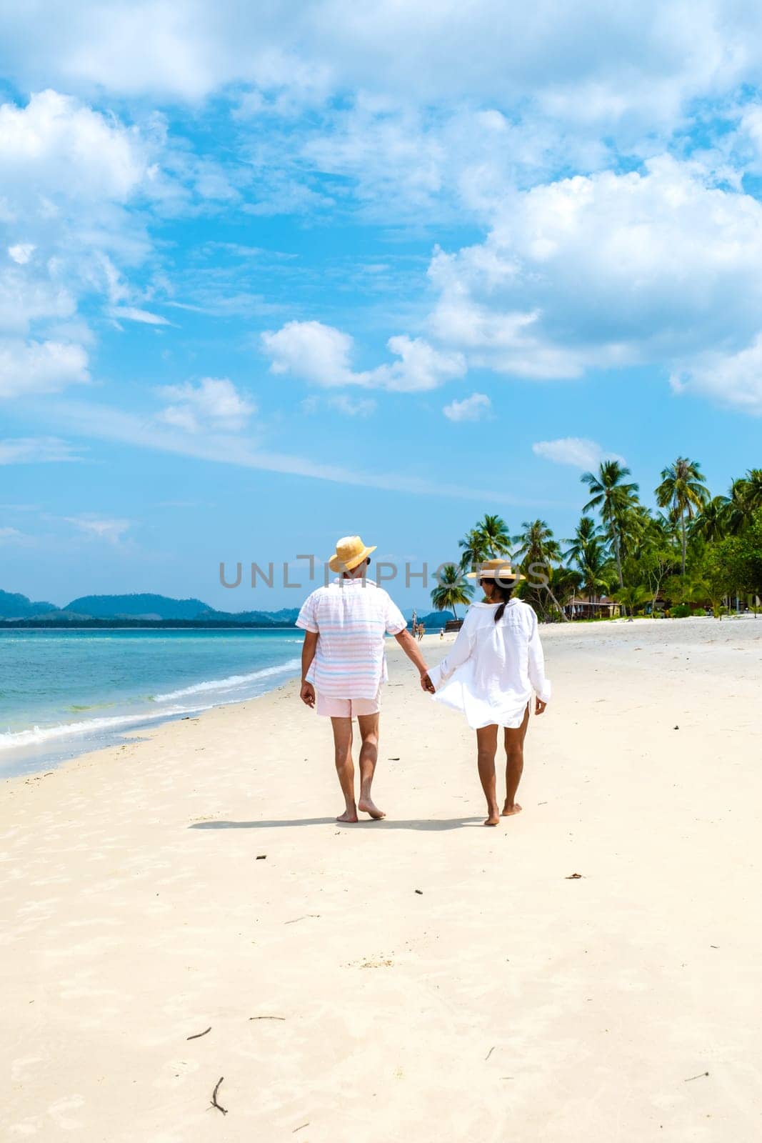 Koh Mook a young couple of caucasian men and Thai Asian woman walking at the beach in Thailand by fokkebok