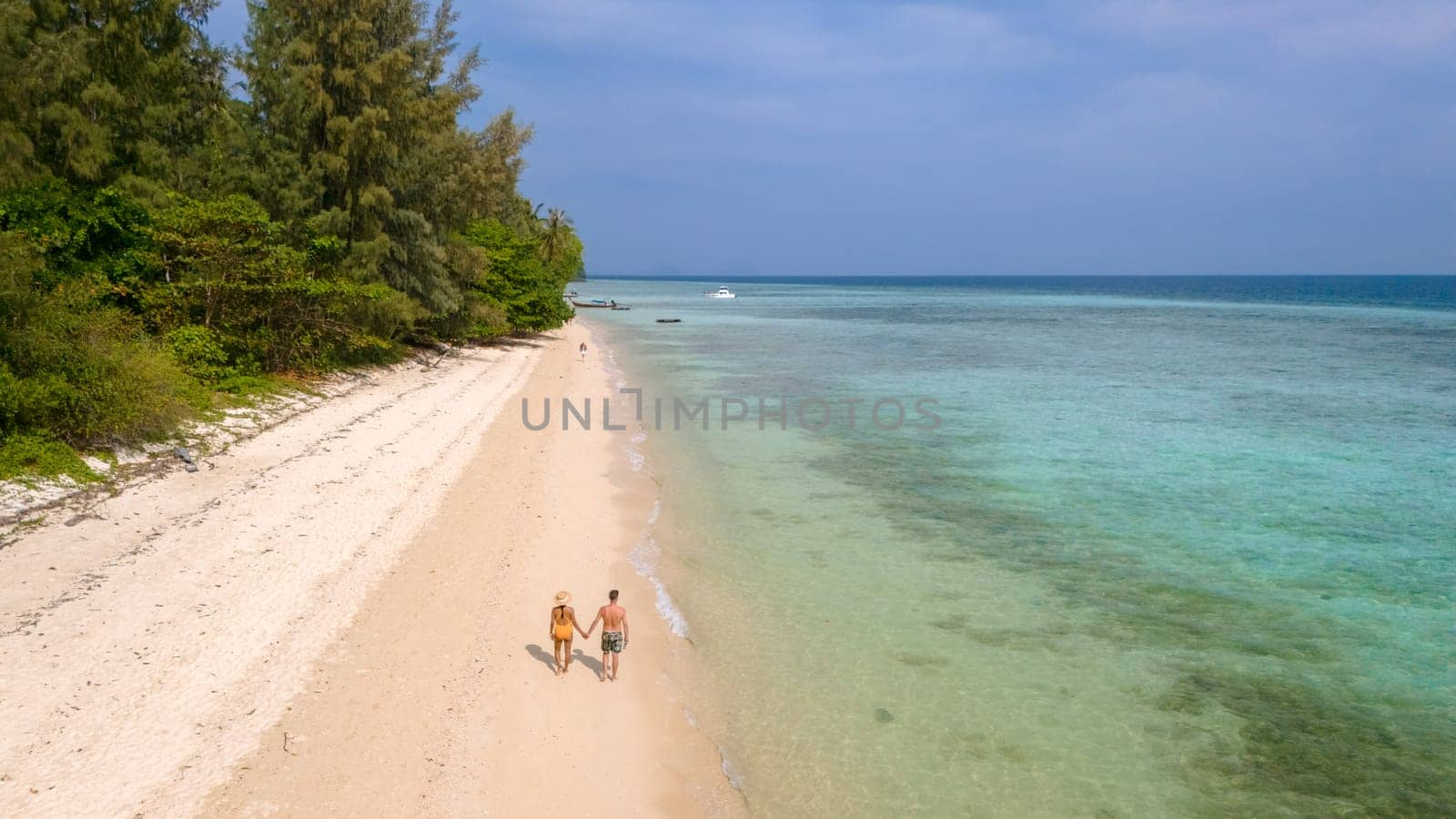 Drone aerial view at Koh Ngai island with palm trees soft white sand, and a turqouse colored ocean in Koh Ngai Trang Thailand, a couple of men and woman walking at tropical beach