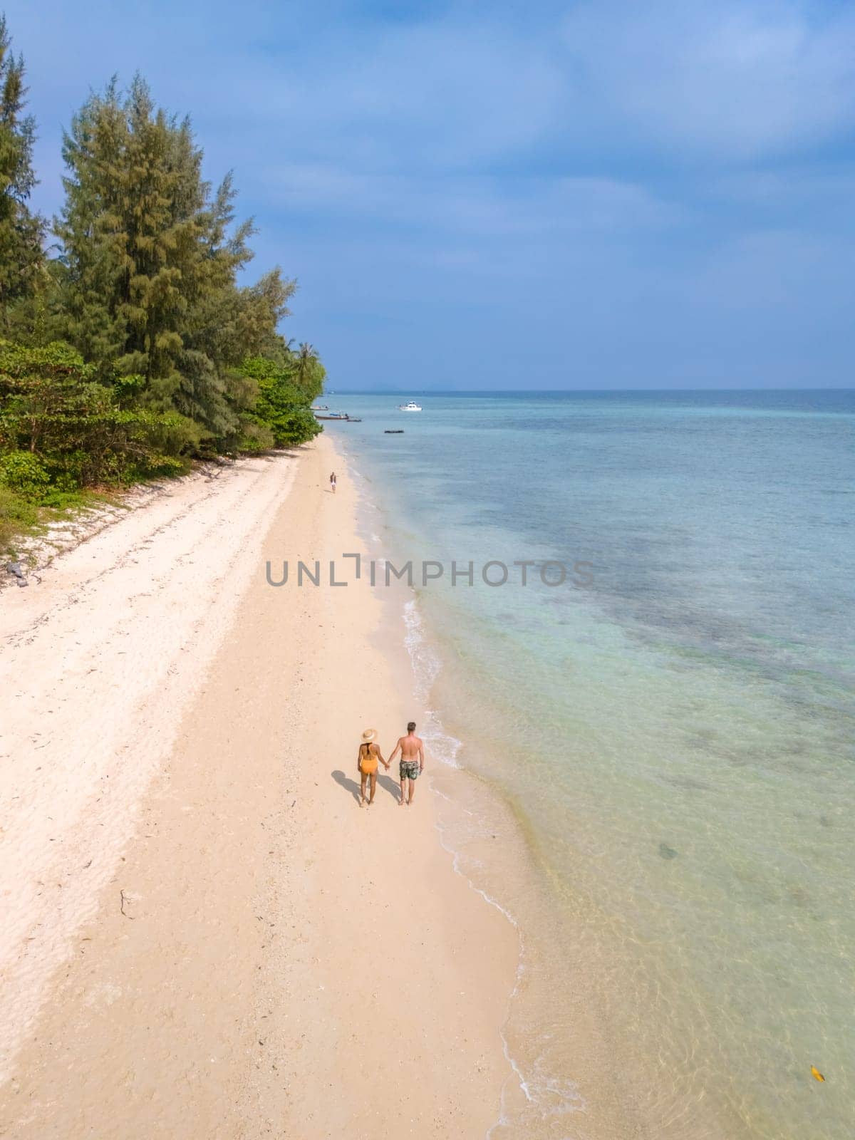 Drone aerial view at Koh Ngai island with palm trees soft white sand, and a turqouse colored ocean in Koh Ngai Trang Thailand, a couple of men and woman walking at tropical beach