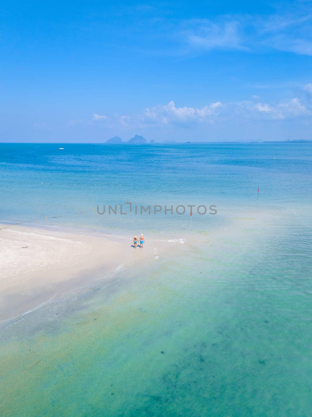 a couple of men and woman walking at the beach during a tropical vacation in Thailand, Koh Muk a tropical island with palm trees soft white sand, and a turqouse colored ocean in Koh Mook Thailand