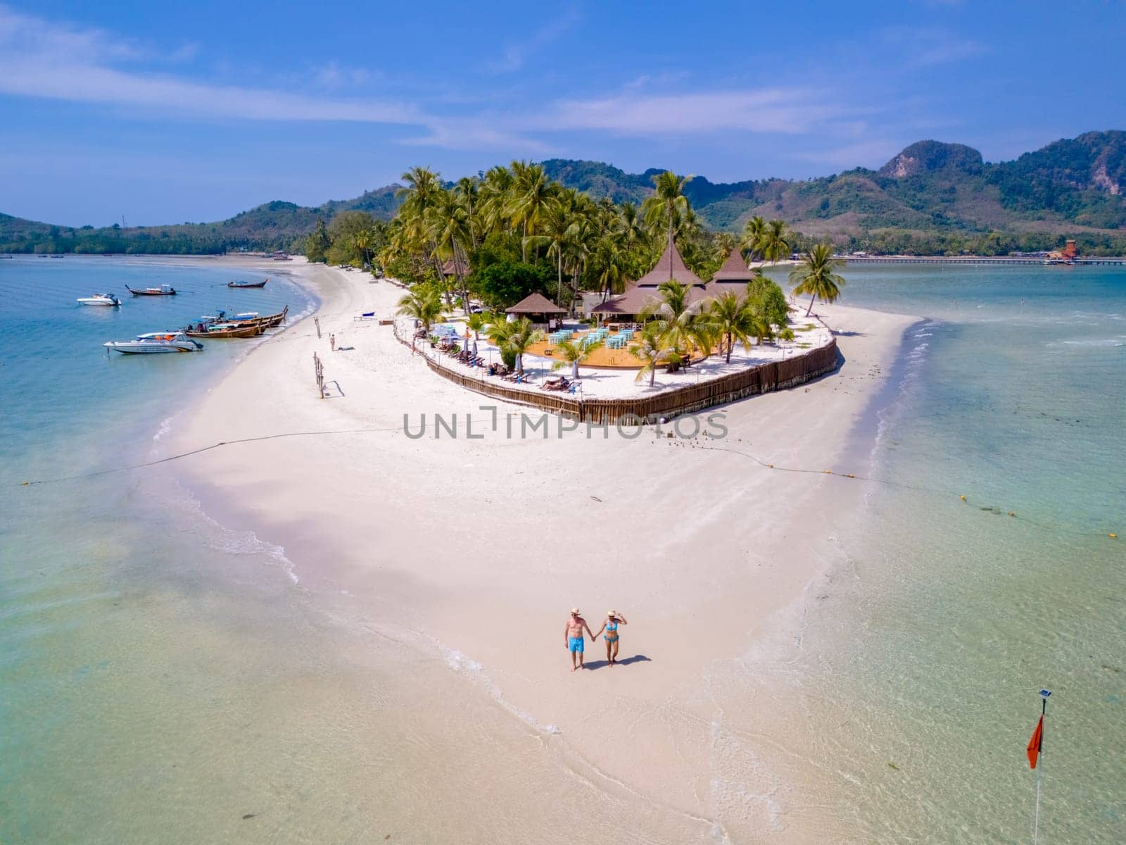 a couple of men and woman walking at the beach during a tropical vacation in Thailand, Koh Muk a tropical island with palm trees soft white sand, and a turqouse colored ocean in Thailand