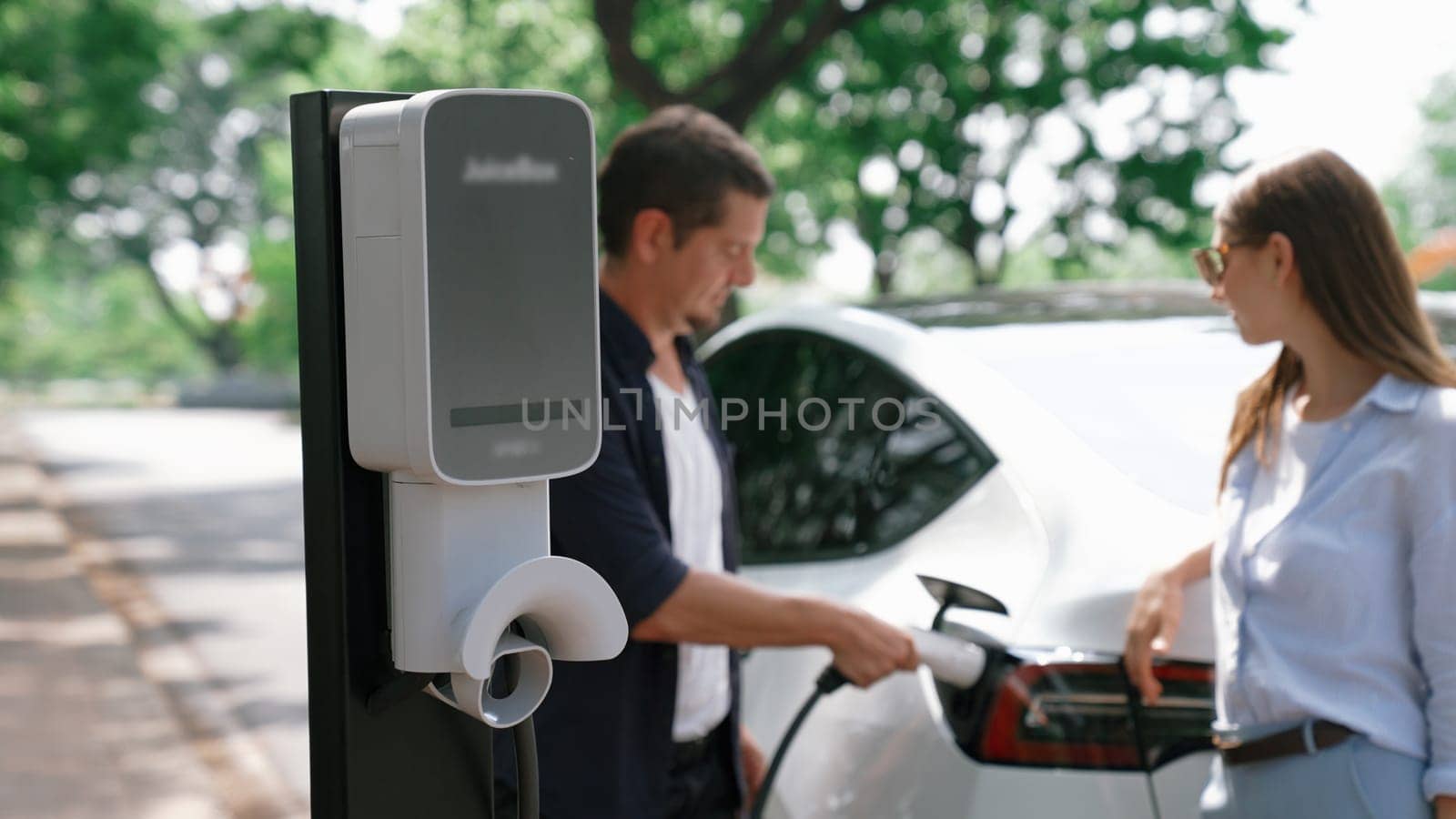 EV car recharging electricity for battery by lovey couple traveling during their road trip travel by eco friendly electric vehicle in national park and greenery forest on holiday. Exalt