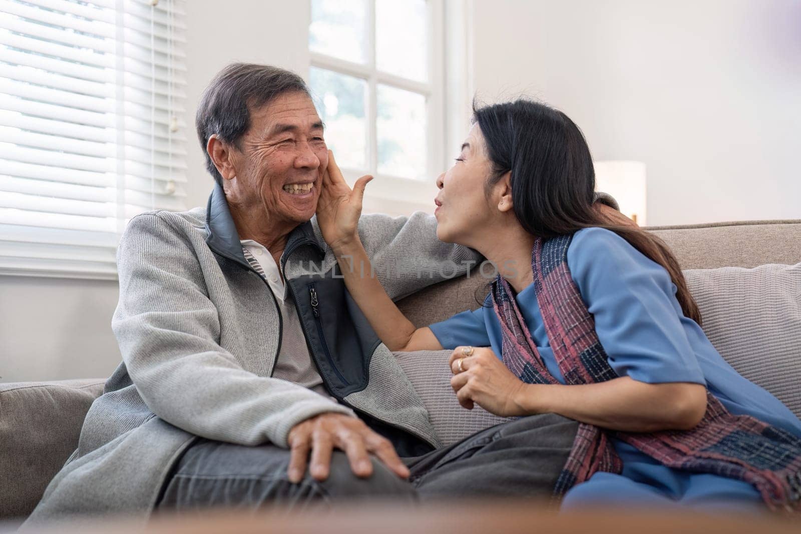 Happy mature husband and wife sit rest on comfortable sofa in living room enjoy talking, smiling elderly couple relax on couch at home chat speak laugh on leisure weekend by nateemee