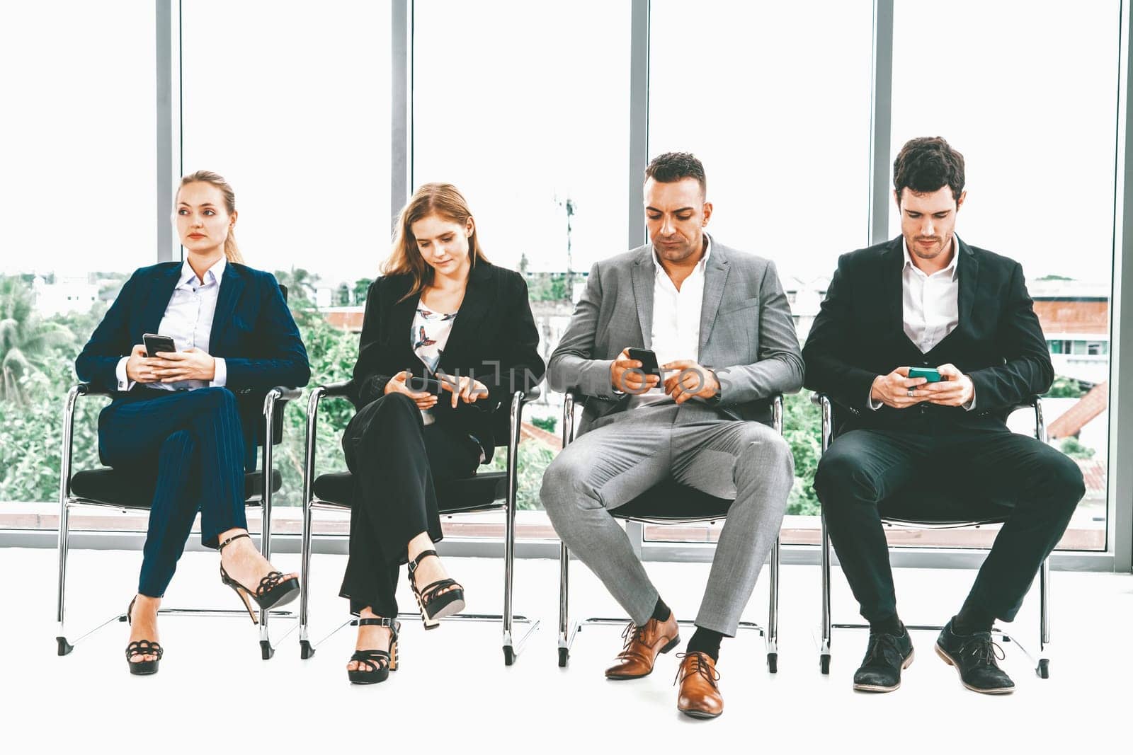 Businesswomen and businessmen using mobile phone while waiting on chairs in office for job interview. Corporate business and human resources concept. uds