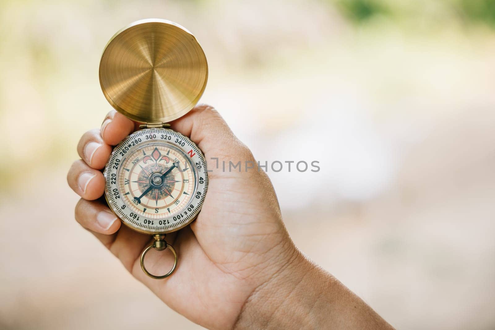 Close-up of a woman's hand holding a compass while hiking in the forest. The compass symbolizes guidance and exploration in the natural environment. by Sorapop
