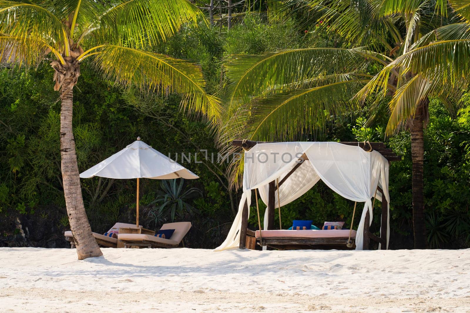 White beach canopies and beach parasol at sunset.Luxury beach tents at luxurious beach resort. Summer beach concept, carefree, rest seaside, Nobody on the beach.Garden on the back.