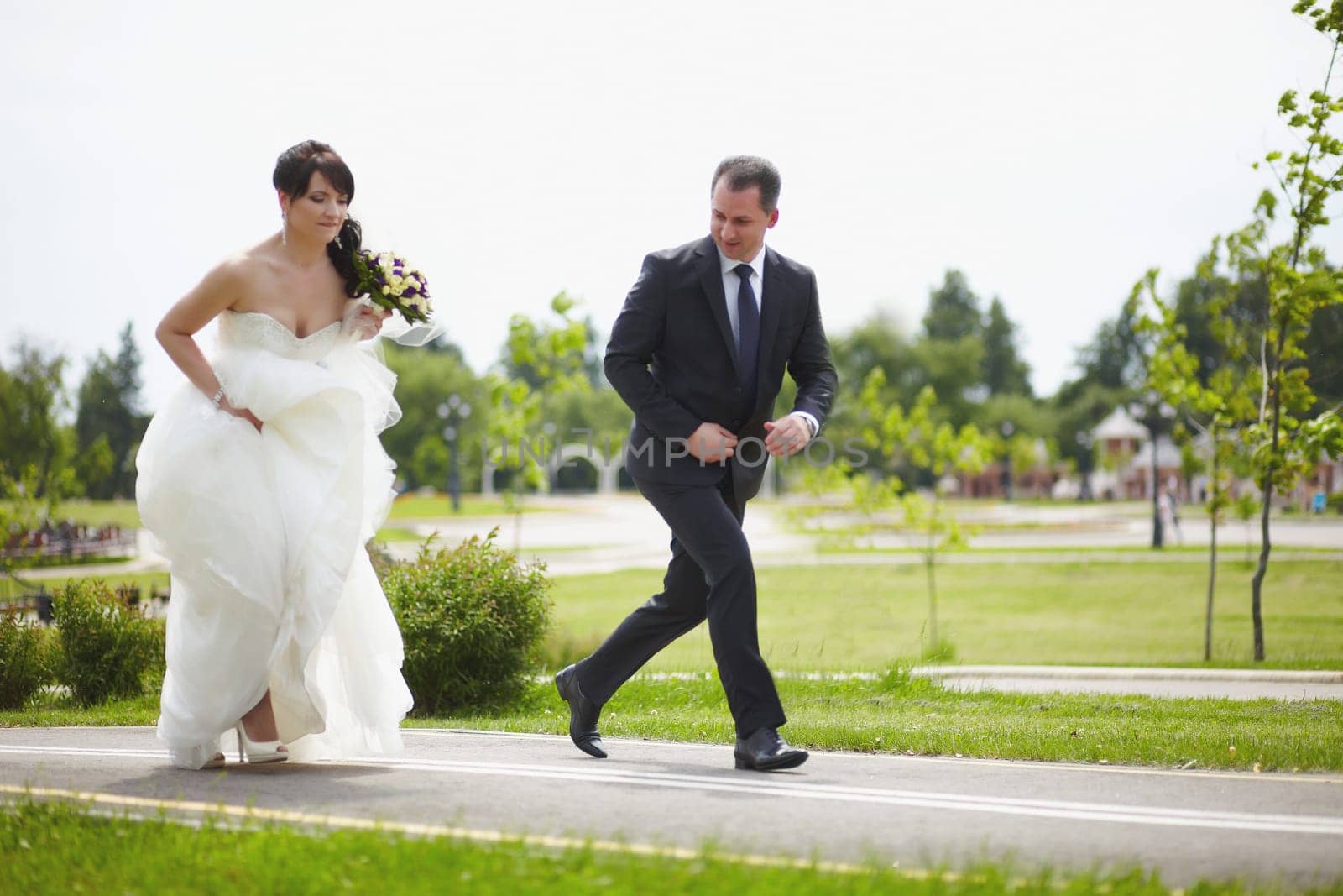 The bride and groom run along the road together by Mastak80