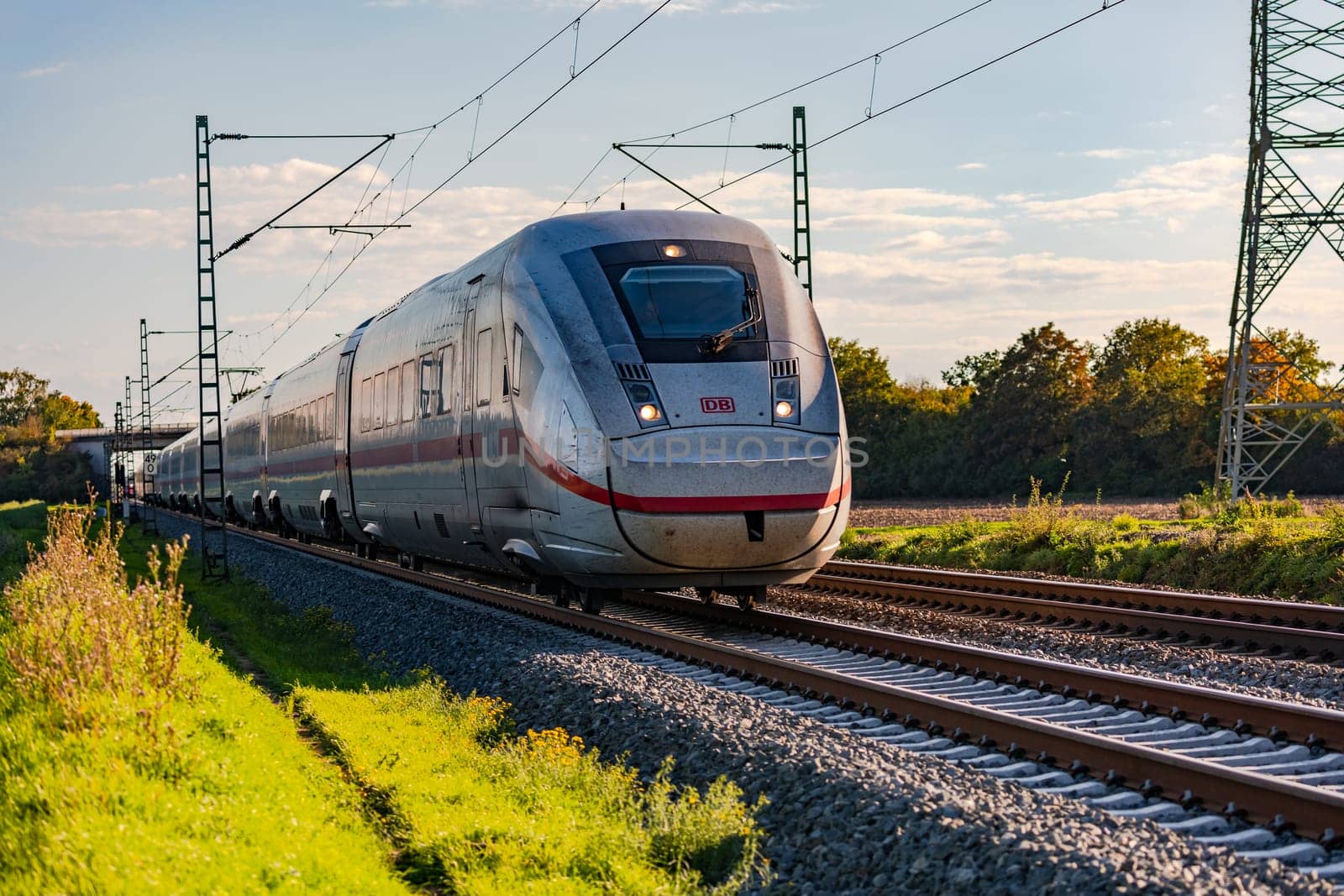 A fast ICE express train runs electrically for passenger transportation through a rural area in Germany