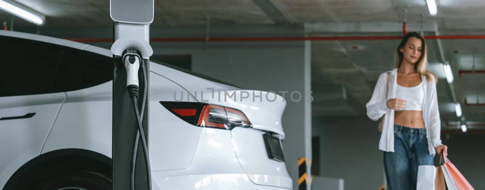 Young woman travel with EV electric car to shopping center parking lot innards by biancoblue