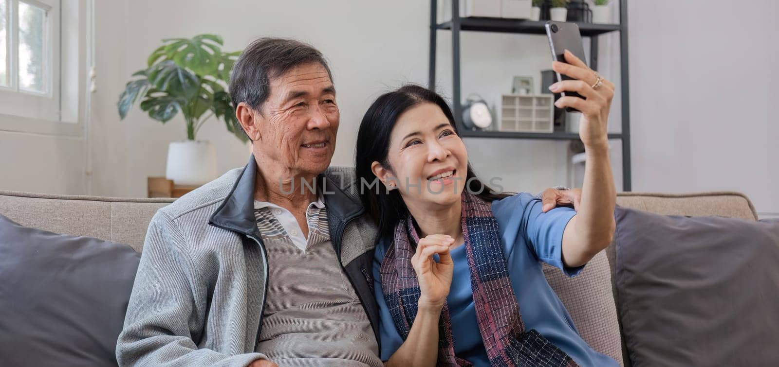 Senior couple in their 60s video chat greeting each other on vacation Have fun together on the sofa in the living room. by wichayada