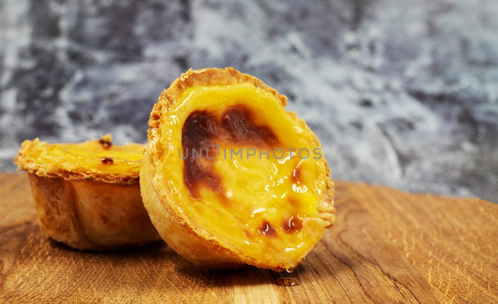 Pastel de nata tarts or Portuguese egg tart on a wooden brown background. Pastel de Belem is a small pie with a crispy puff pastry crust and a custard cream filling. Sweet dessert. by Roshchyn