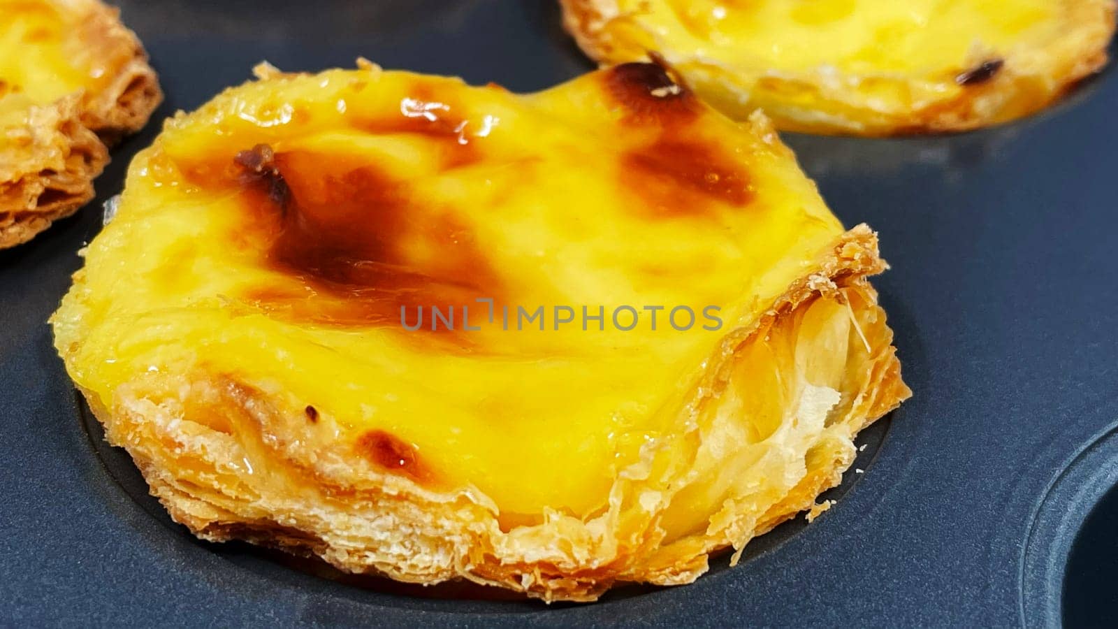 Lots of freshly baked Pastel de nata or Portuguese egg tart desserts in a baking dish. Pastel de Belme is a small pie with a crispy puff pastry crust and a custard filling. Small cupcake. by Roshchyn