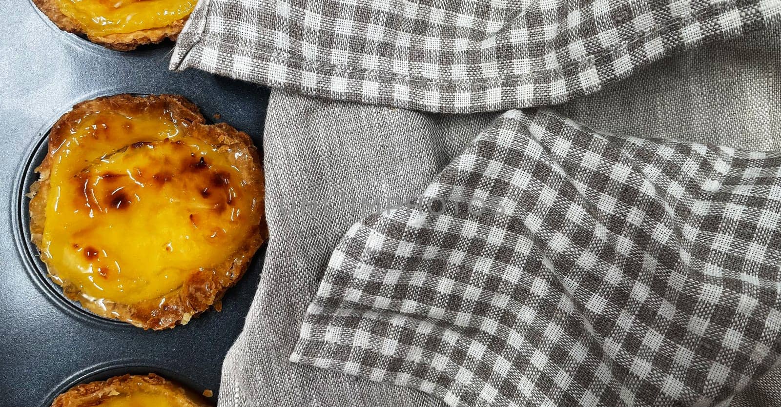 Lots of freshly baked Pastel de nata or Portuguese egg tart desserts in a baking dish. Pastel de Belme is a small pie with a crispy puff pastry crust and a custard filling. Small cupcake