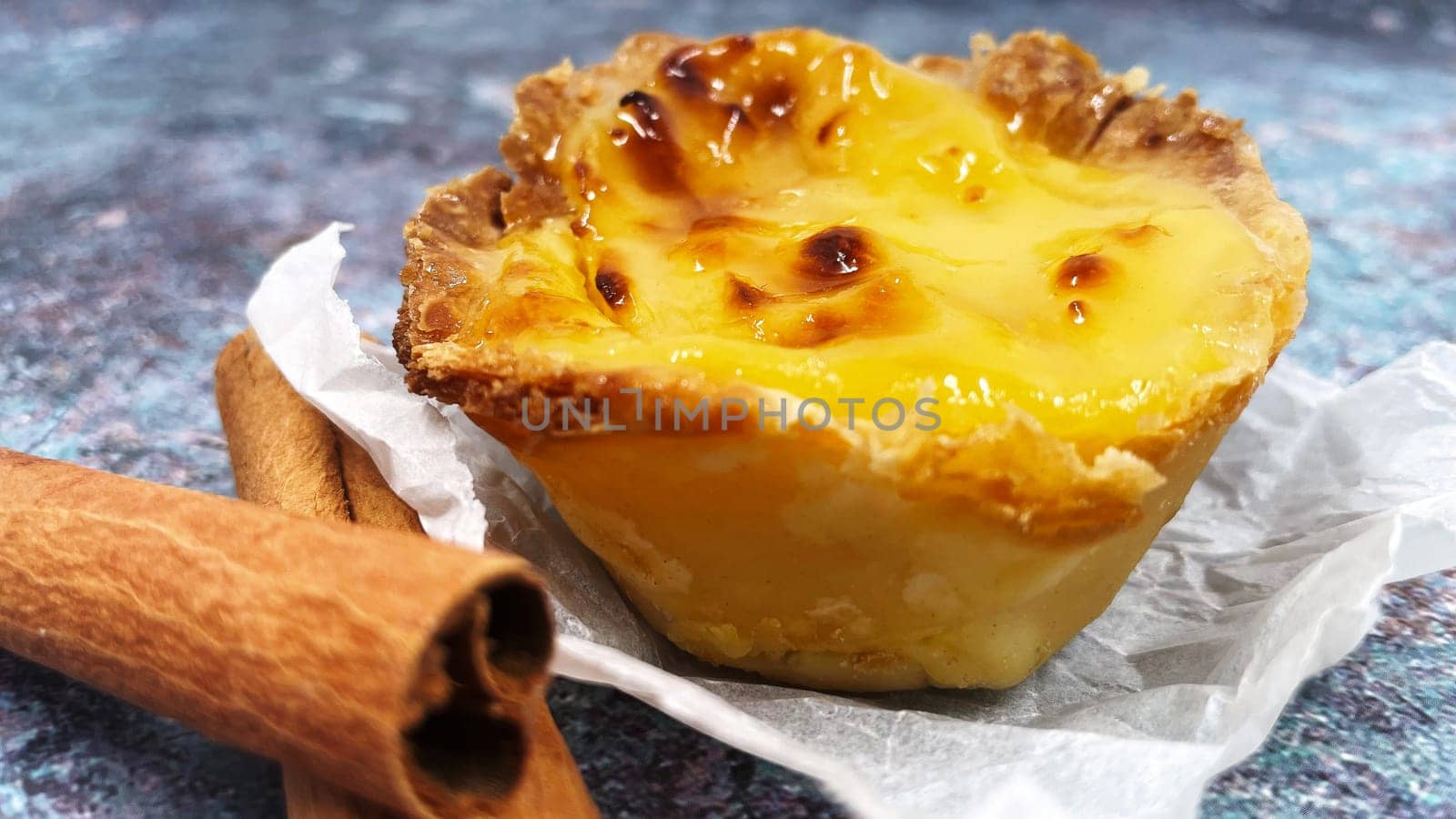 One Pastel de nata or Portuguese egg tart and cinnamon sticks. Pastel de Belm is a small pie with a crispy puff pastry crust and a custard cream filling