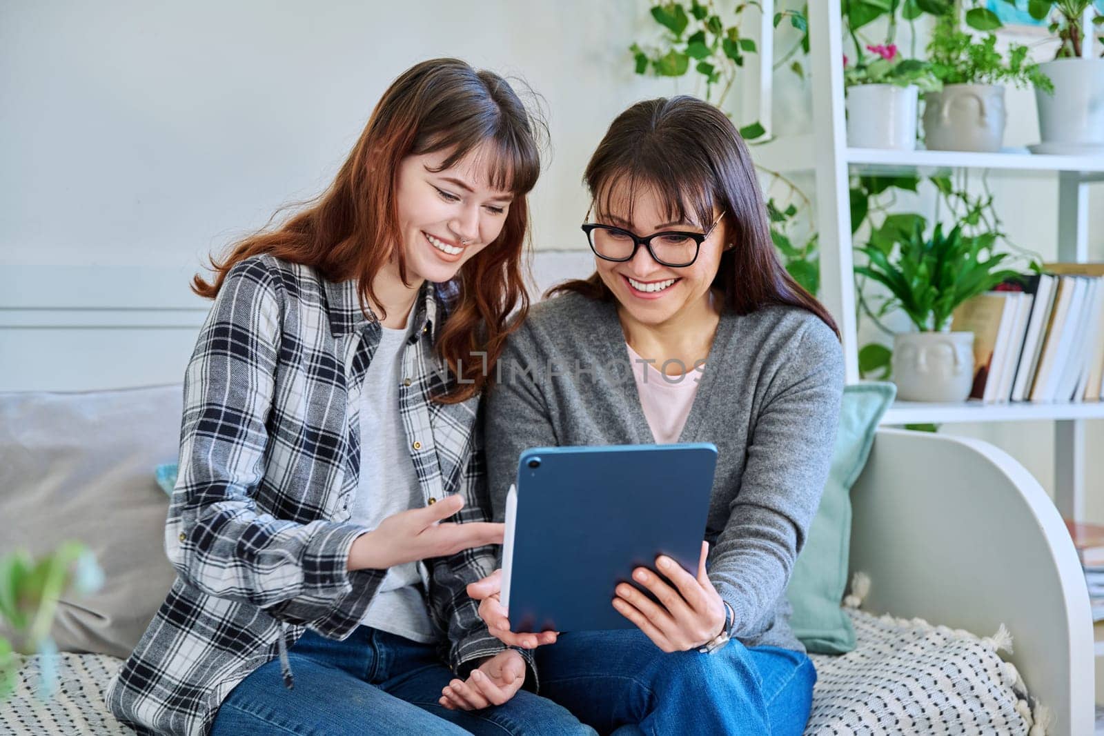 Happy mother and teenage daughter looking together at screen of digital tablet by VH-studio