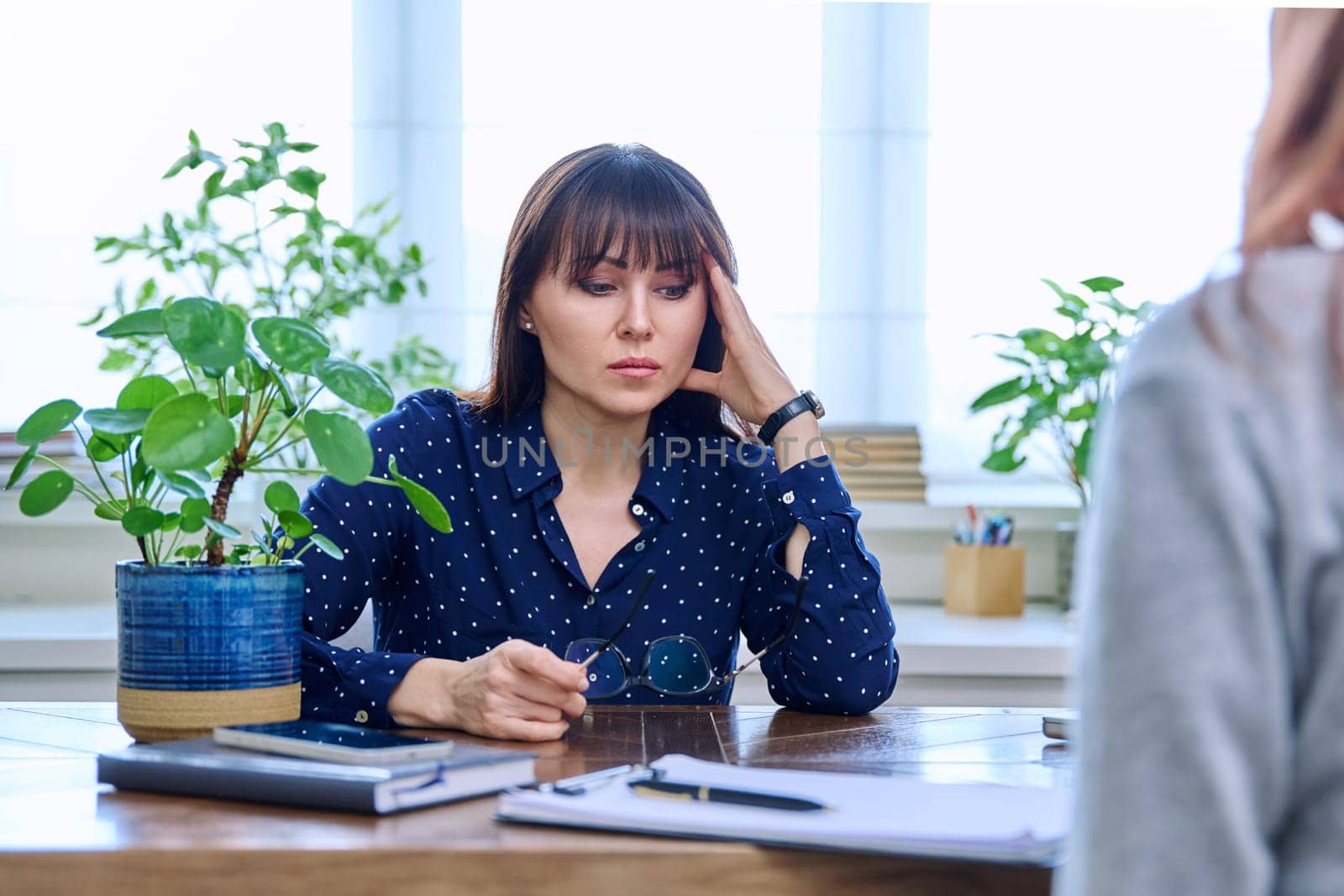 Mature sad woman in therapy session with mental professional psychologist, sitting at table in office of therapist counselor social worker. Psychology psychotherapy mental assistance treatment support