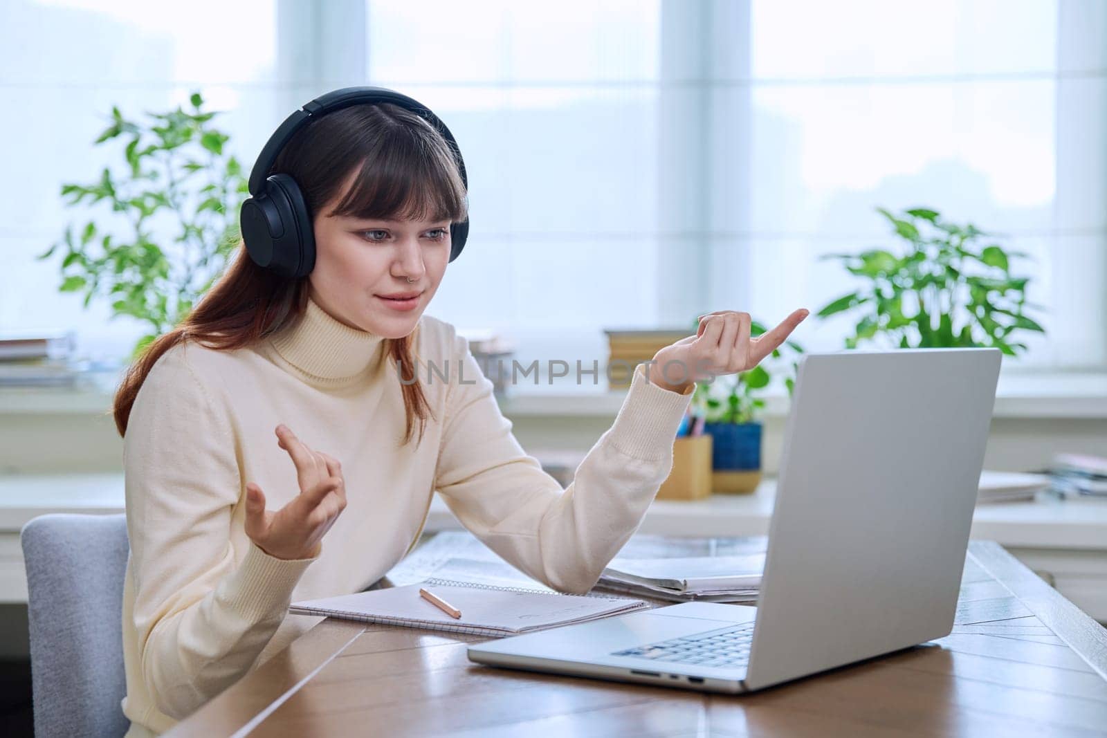 Teenage girl college student in headphones having video conference chat online meeting lesson webinar on computer laptop screen, sitting at desk at home. E-learning, education, technology, knowledge