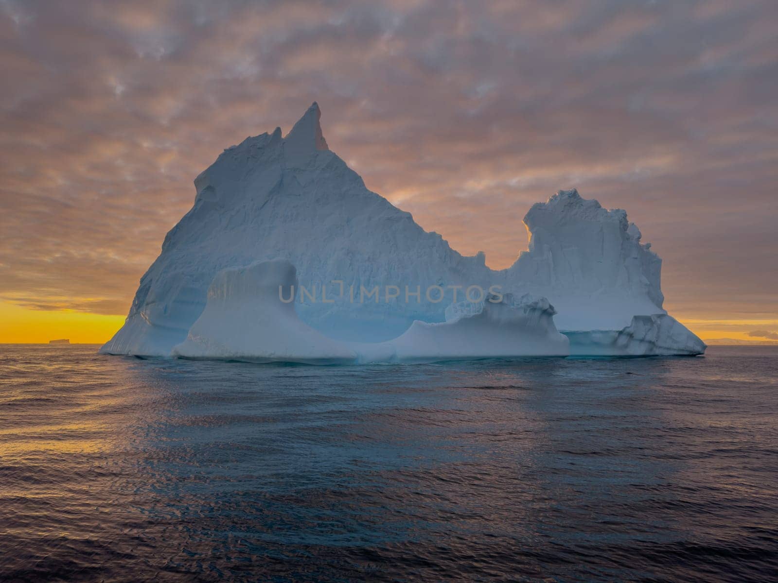 A huge high breakaway glacier drifts in the southern ocean off the coast of Antarctica at sunset, the Antarctic Peninsula, the Southern Arctic Circle, azure water, cloudy weather by vladimirdrozdin