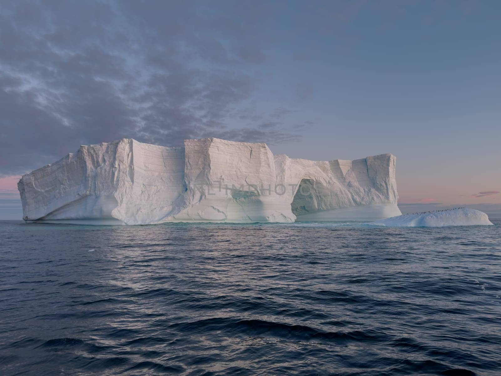 A huge high breakaway glacier drifts in the southern ocean off the coast of Antarctica at sunset, the Antarctic Peninsula, the Southern Arctic Circle, azure water, cloudy weather by vladimirdrozdin