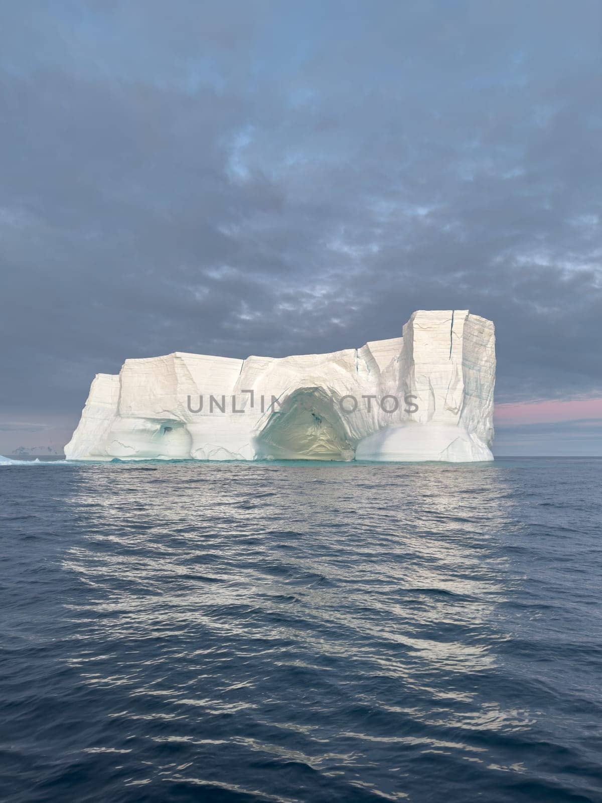 A huge high breakaway glacier drifts in the southern ocean off the coast of Antarctica at sunset, the Antarctic Peninsula, the Southern Arctic Circle, azure water, cloudy weather by vladimirdrozdin