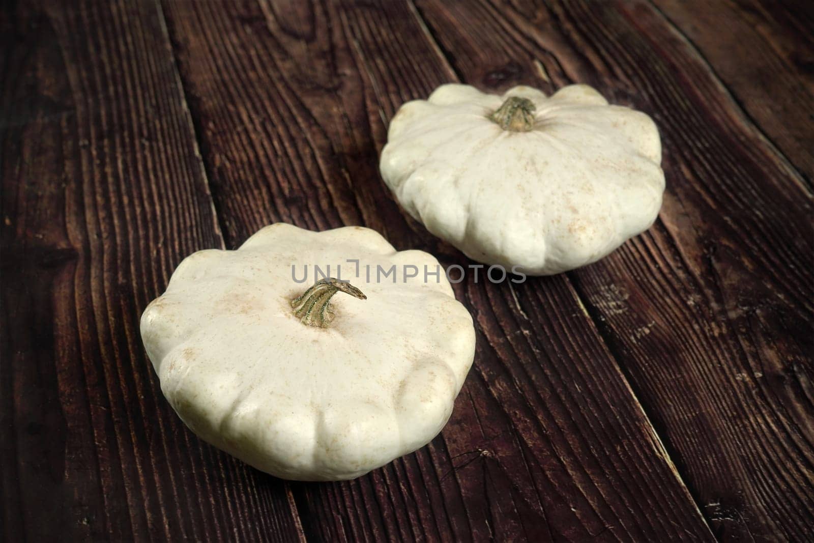 Two white pattypan squash on dark wooden board by Ivanko