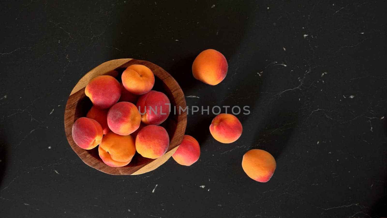 Top down view, small wooden bowl with apricots, some spilled on dark marble like board under by Ivanko