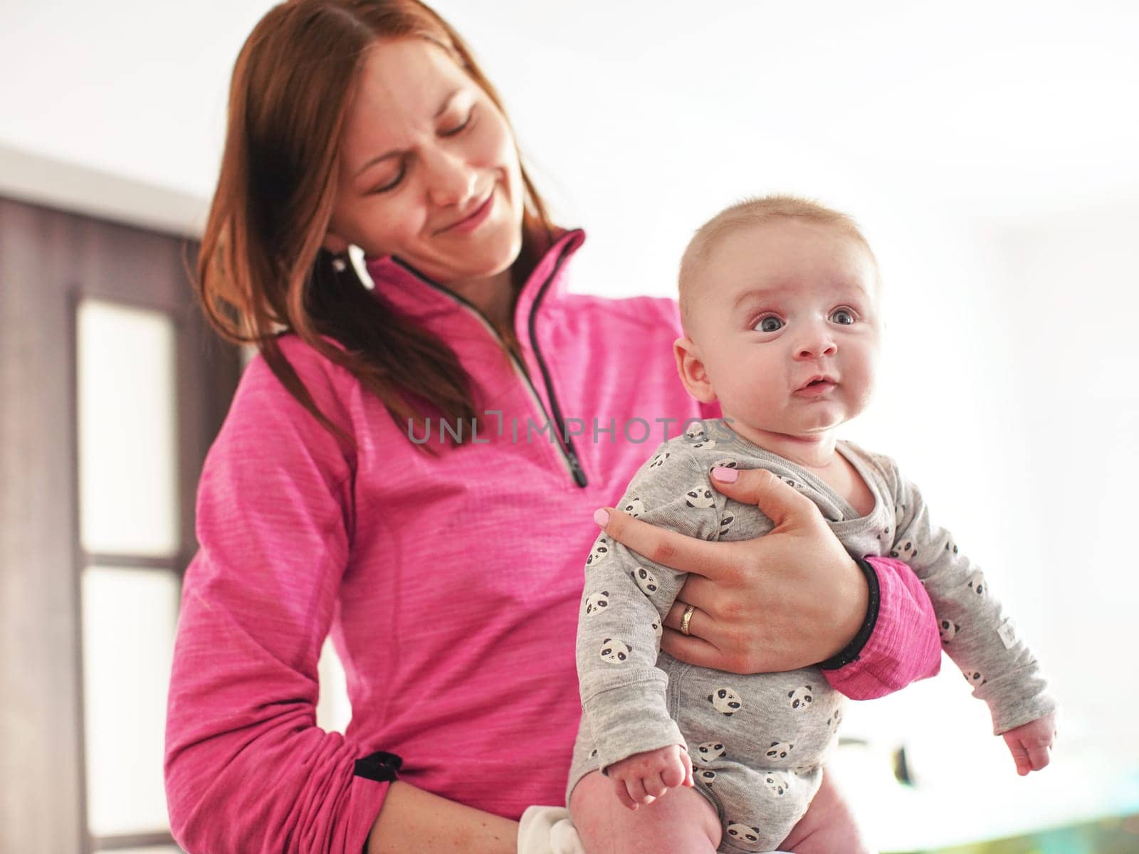 Mother holds infant baby boy son in her hands, as she plays with him by Ivanko