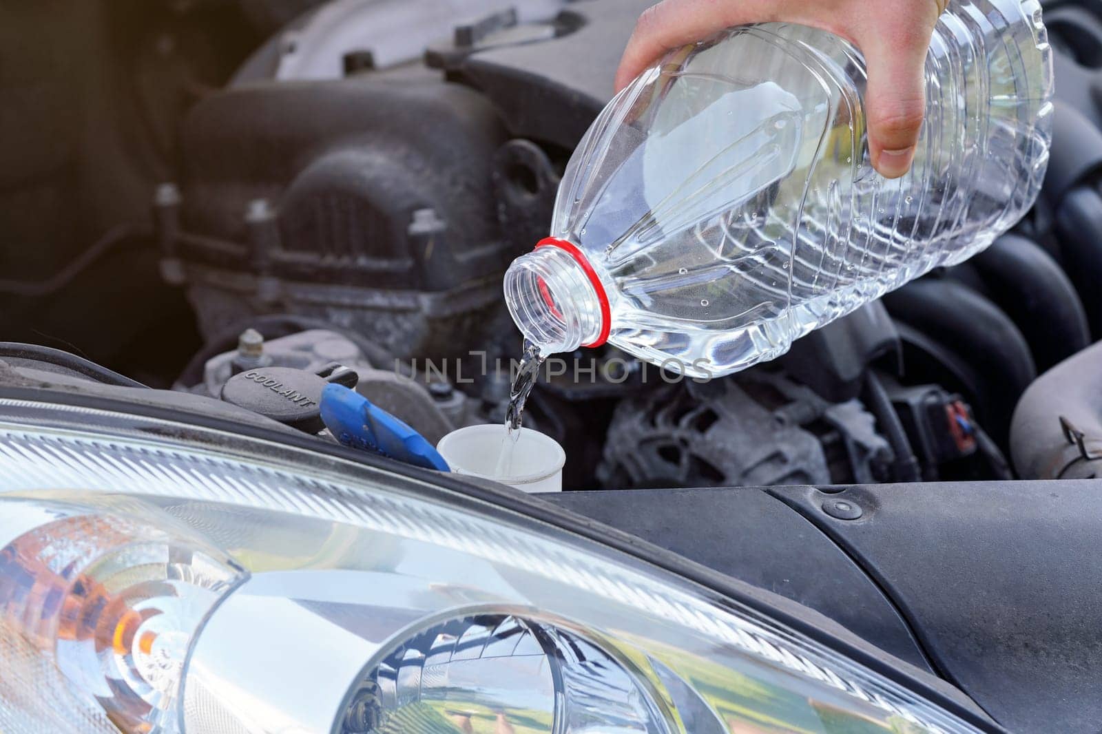 Man pouring distilled water (ecological alternative to washing fluid) to washer tank in car, detail on hand holding clear plastic bottle by Ivanko