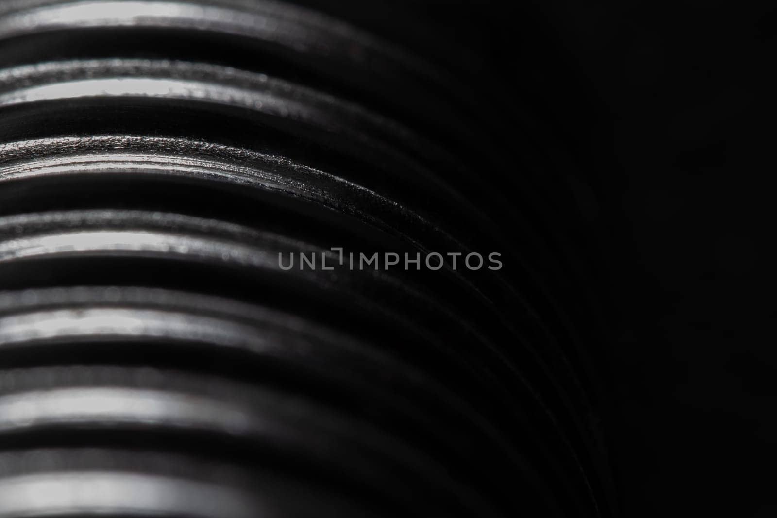 Close up of the thread of a metallic screw on black background, textured metal, abstract macro