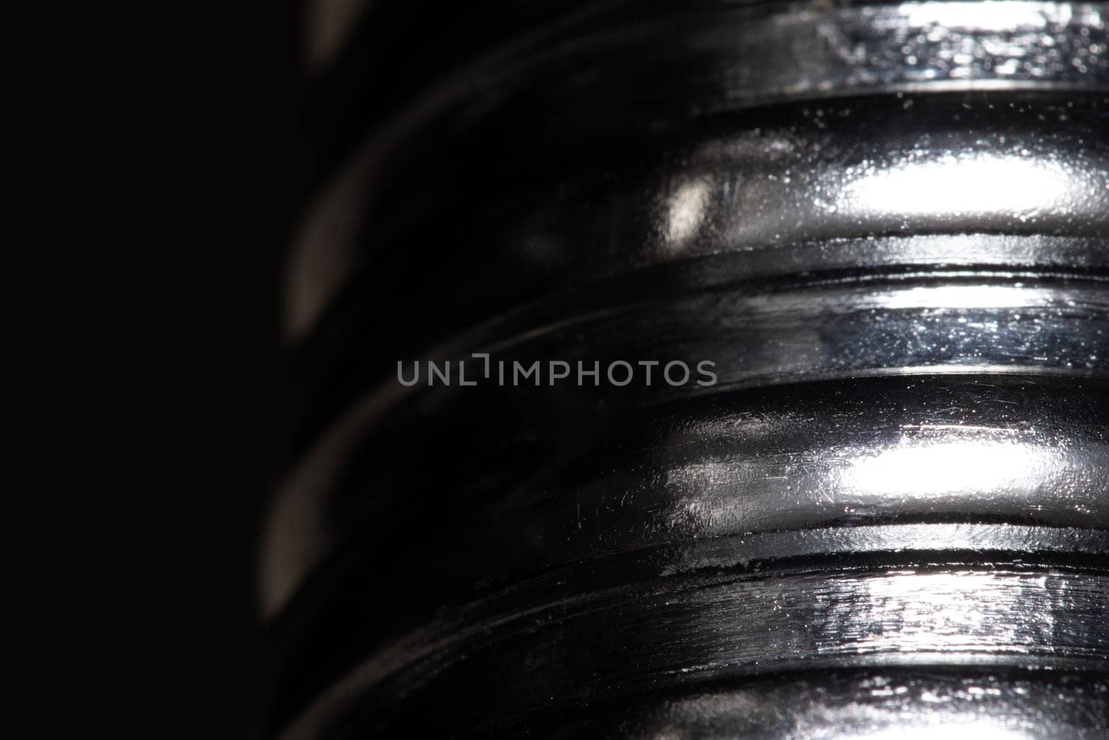 Close up of the thread of a metallic screw on black background, textured metal, abstract macro