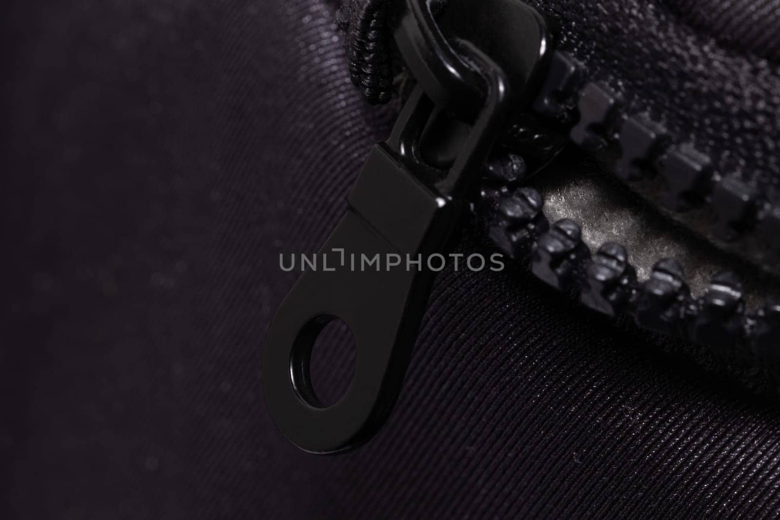 This image captures the detailed texture of a black zipper partially closed on a dark fabric, highlighting the interlocking teeth and the metal pull.