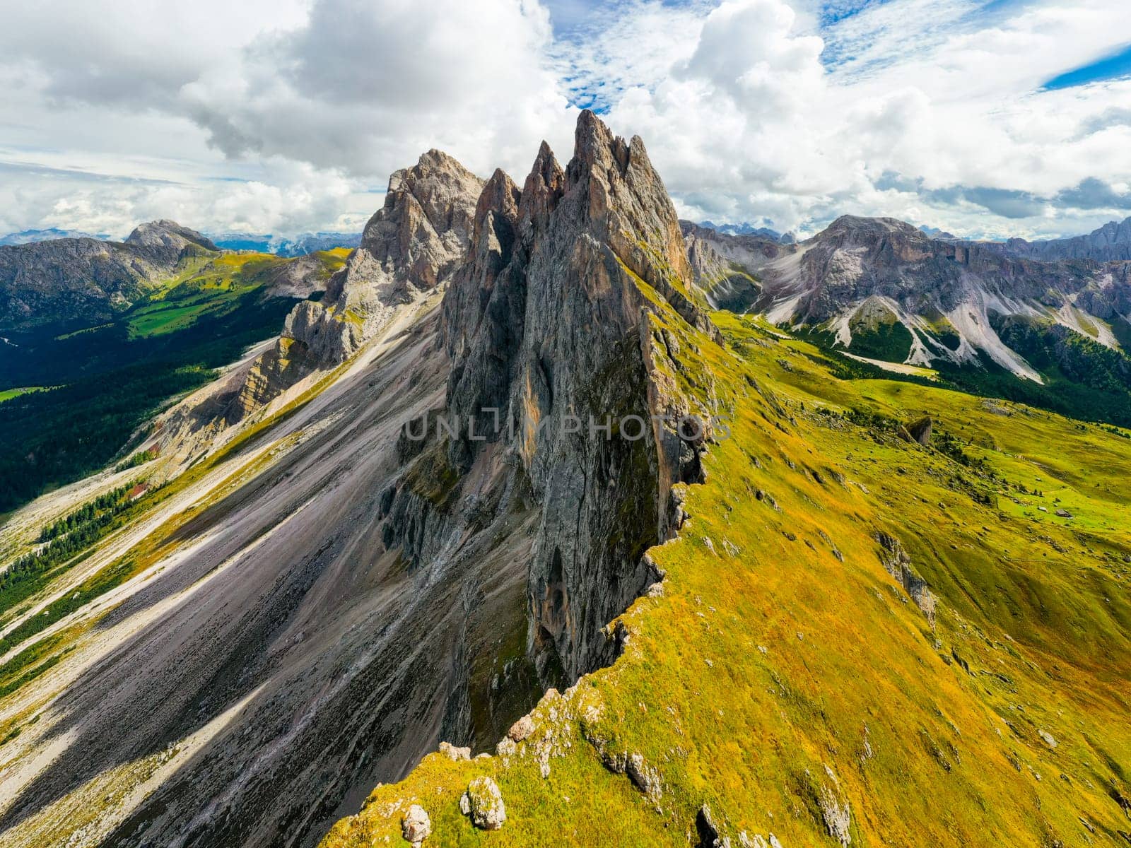 Observation point facing giant Seceda mountain in Italian Alps. Rocky ridgeline in highland under cloudy sky on summer day aerial view