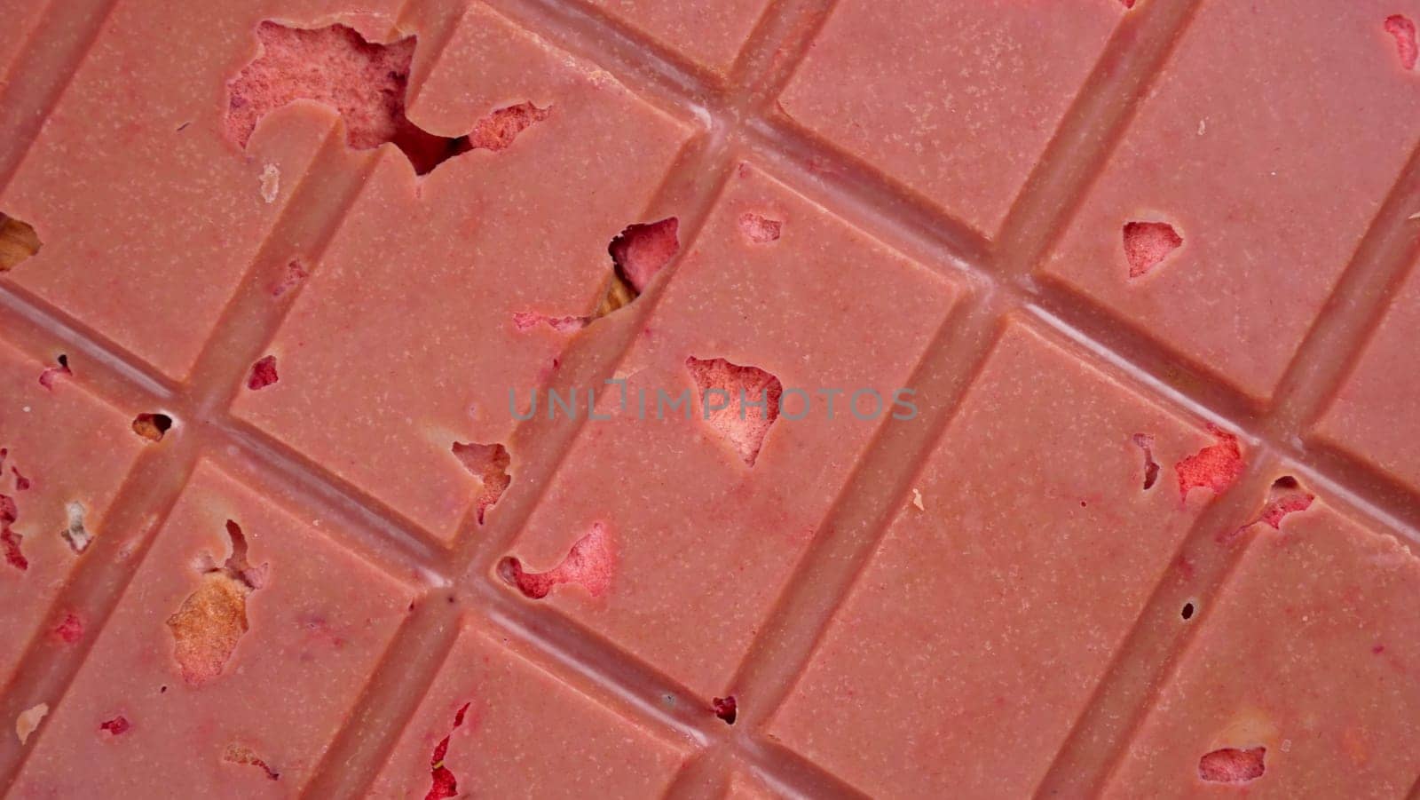 A bar of pink ruby chocolate with freeze-dried strawberries and almonds close-up. A healthy dessert based on berries and nuts