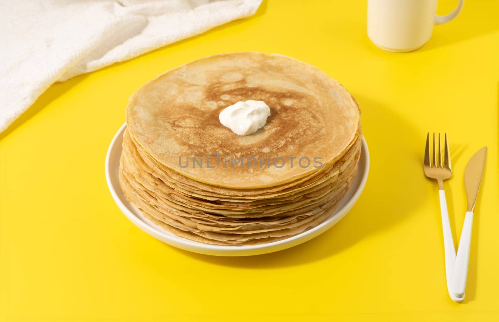 A stack of thin pancakes on a yellow table.