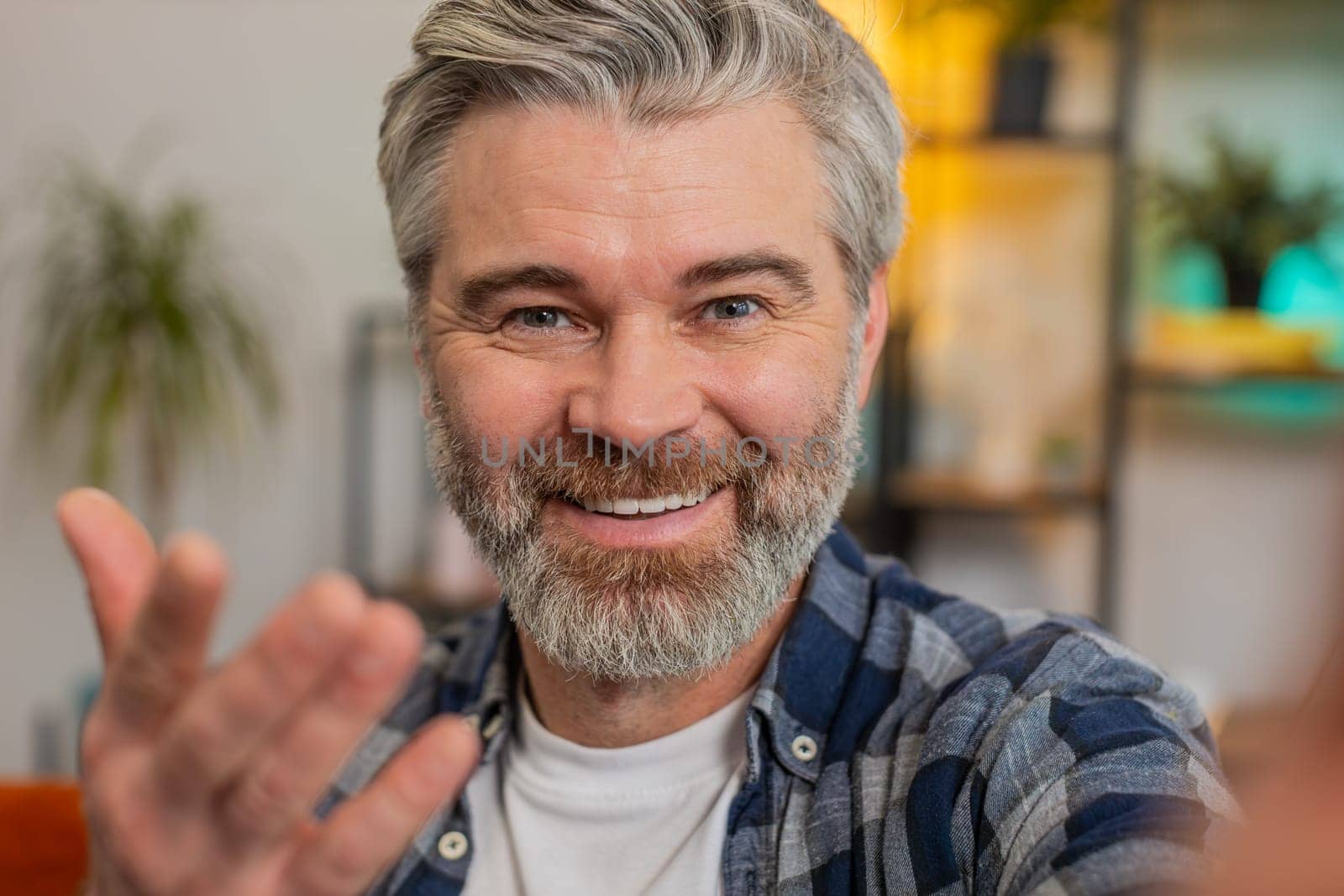 POV portrait of happy senior man in casuals chatting with friend or relative on video online call. Cheerful grey-haired Caucasian middle-aged blogger guy waving goodbye while recording vlog at home