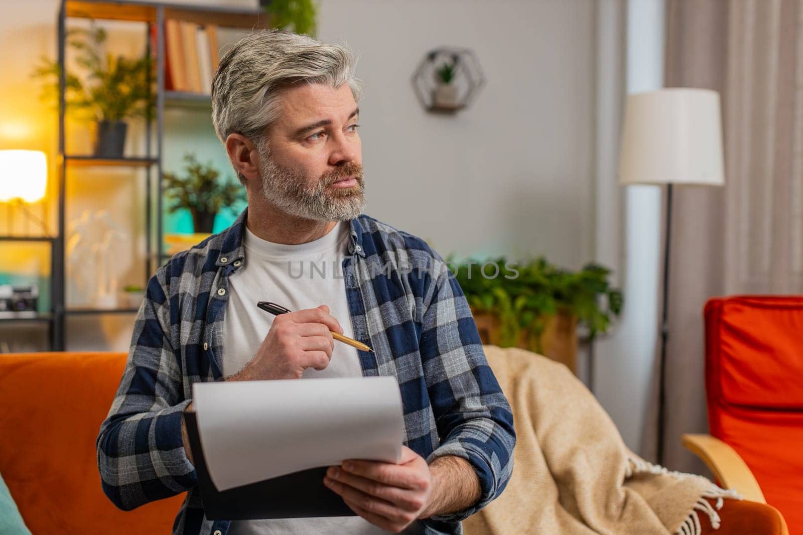 Confident bearded mature man in casual clothes with documents analyzing information reading business papers prepare financial report. Senior Caucasian old guy shocked by sudden victory success on sofa