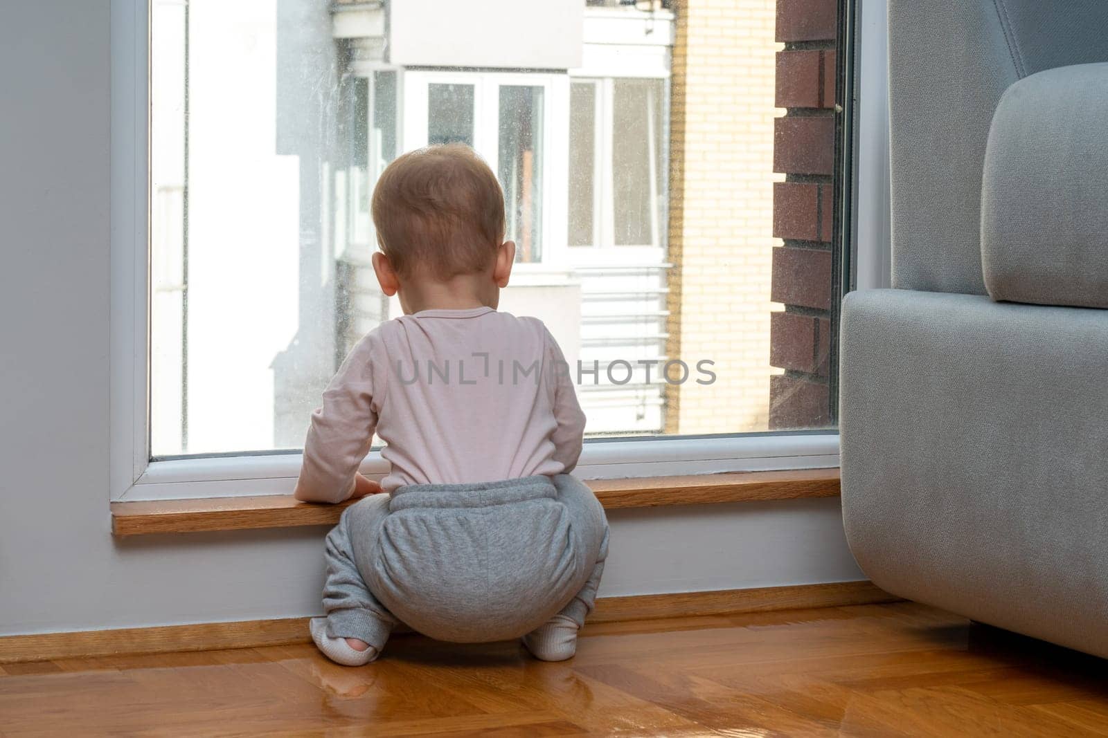 Baby waits by the window for dad to come home. Concept of family and longing by Mariakray