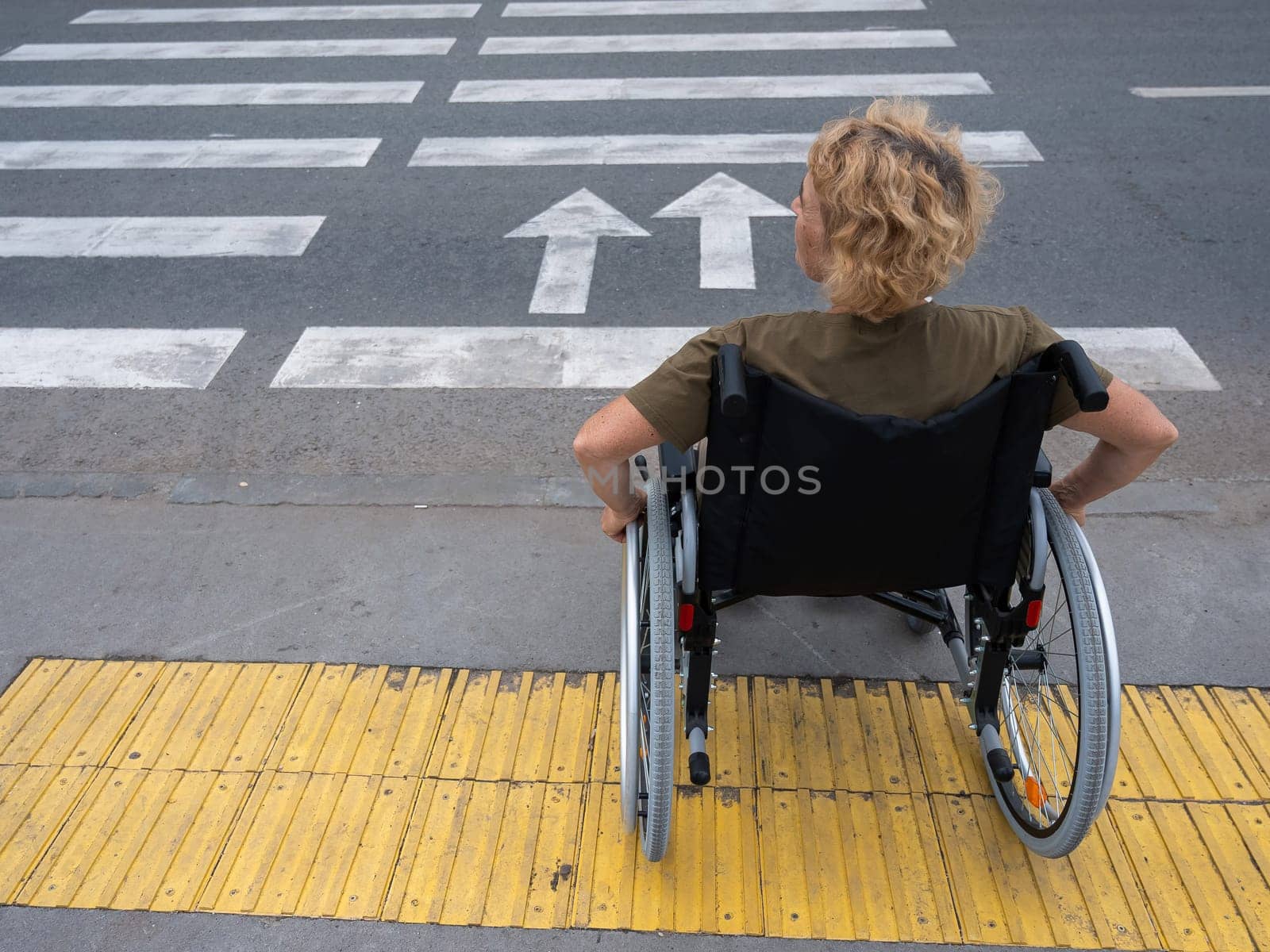 Rear view of an elderly woman on a wheelchair going to a pedestrian crossing
