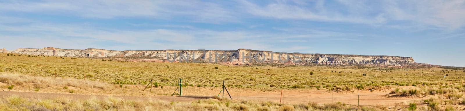 Panoramic view of majestic mesa formations under clear blue sky in Sedona, Arizona, with sparse desert vegetation and a boundary fence