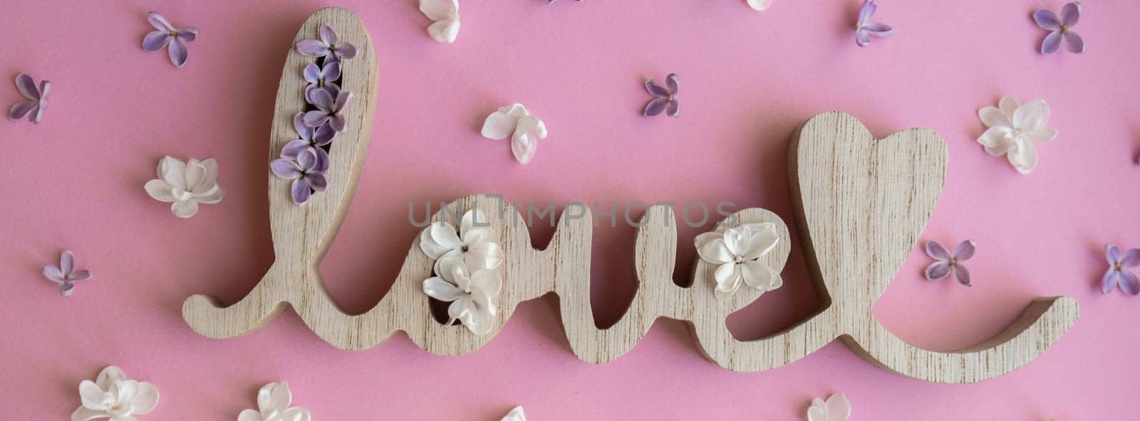 Wooden word LOVE and lilac flowers on pink purple background. St. Valentine Day, love or wedding day concept. Romantic background composition. Pastel Light Pink Lilac Flower Bunch Wallpaper greeting card