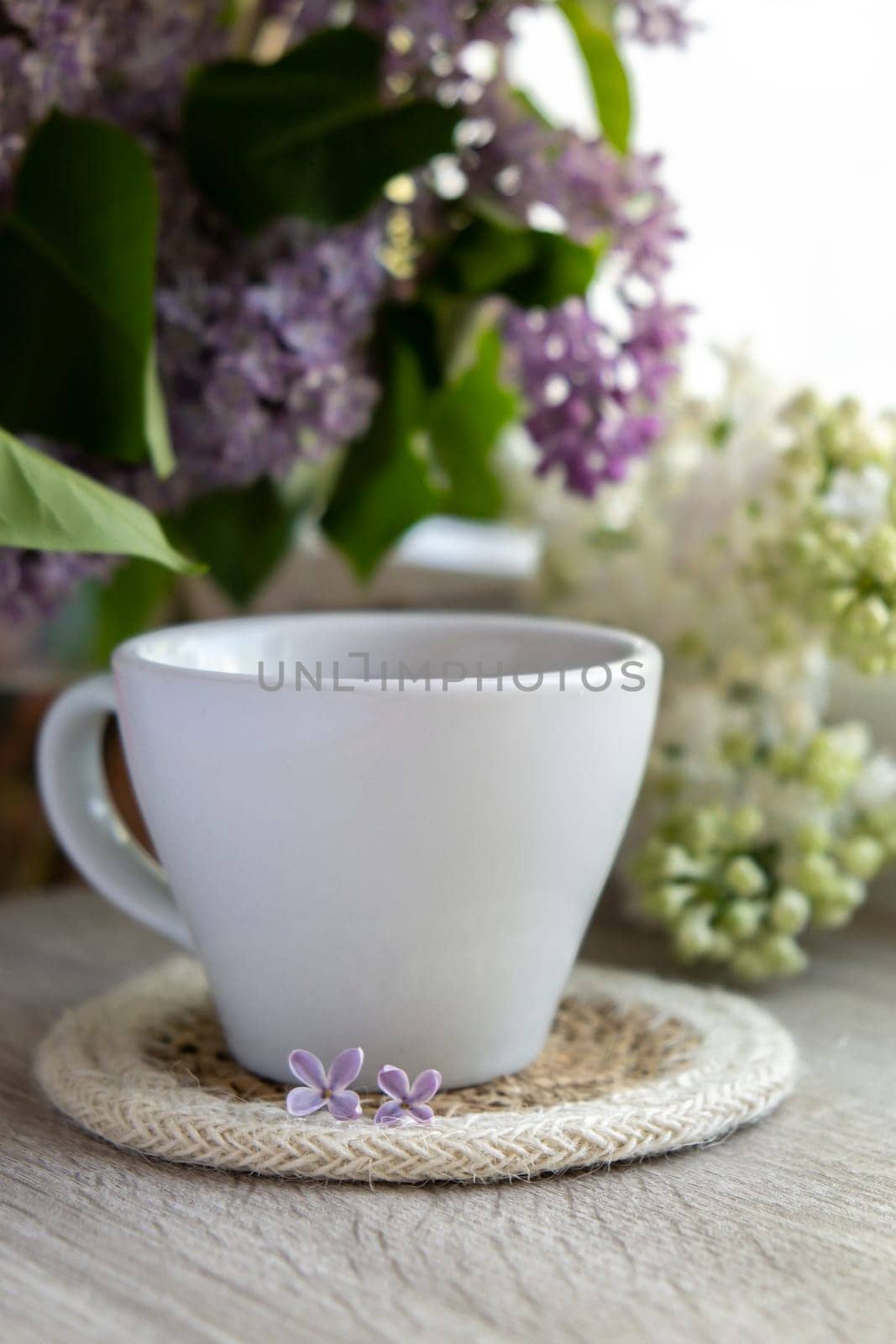 Tasty black tea in white cup on windowsill with aromatic lilac flowers. Spring composition Cup of lilac tea drinking recipe flowering branches of purple lilac. Still life for copy space greeting card, poster, banner, wallpaper. Relaxation and natural ingredients
