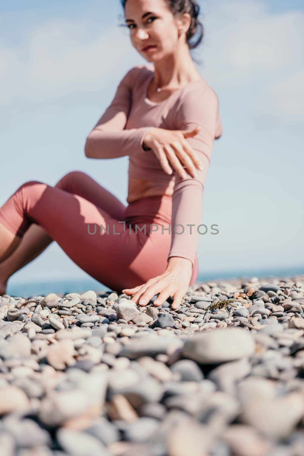 Young woman with long hair in white swimsuit and boho style braclets practicing outdoors on yoga mat by the sea on a sunset. Women's yoga fitness routine. Healthy lifestyle, harmony and meditation